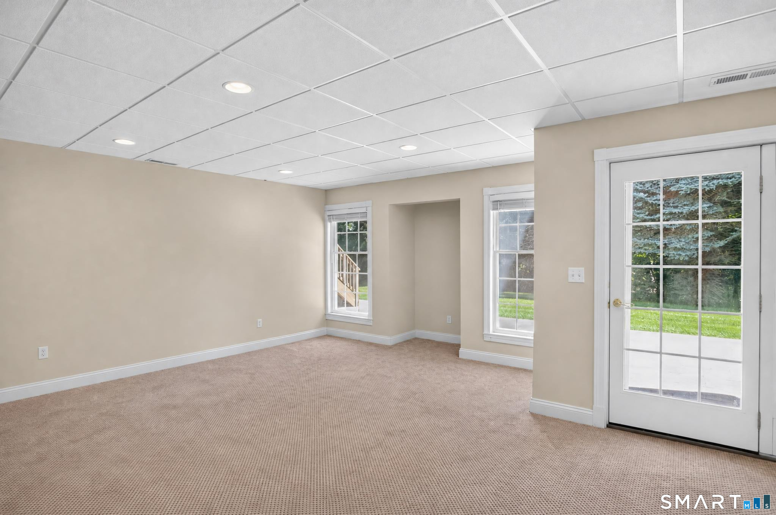 Empty carpeted room with two windows and a glass-paneled door to the patio.