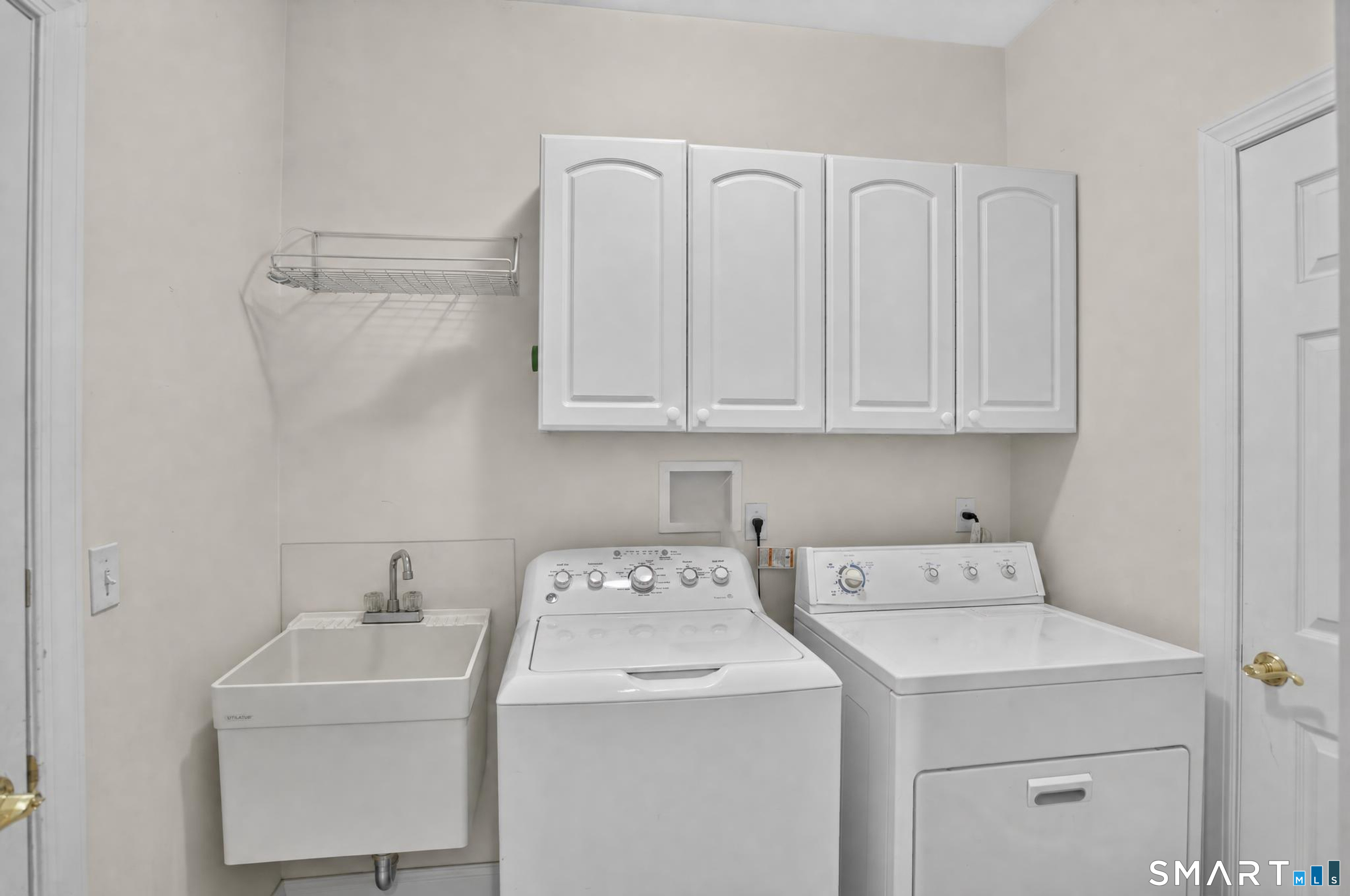 Laundry room with a utility sink, washer, dryer, and overhead cabinets.