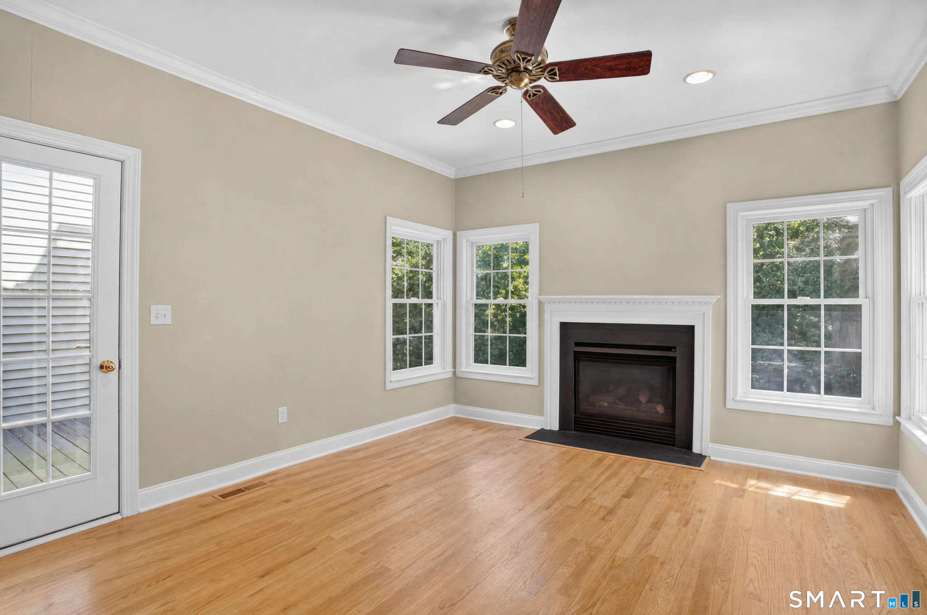 Unfurnished living room with hardwood floors, a fireplace, ceiling fan, and multiple windows.