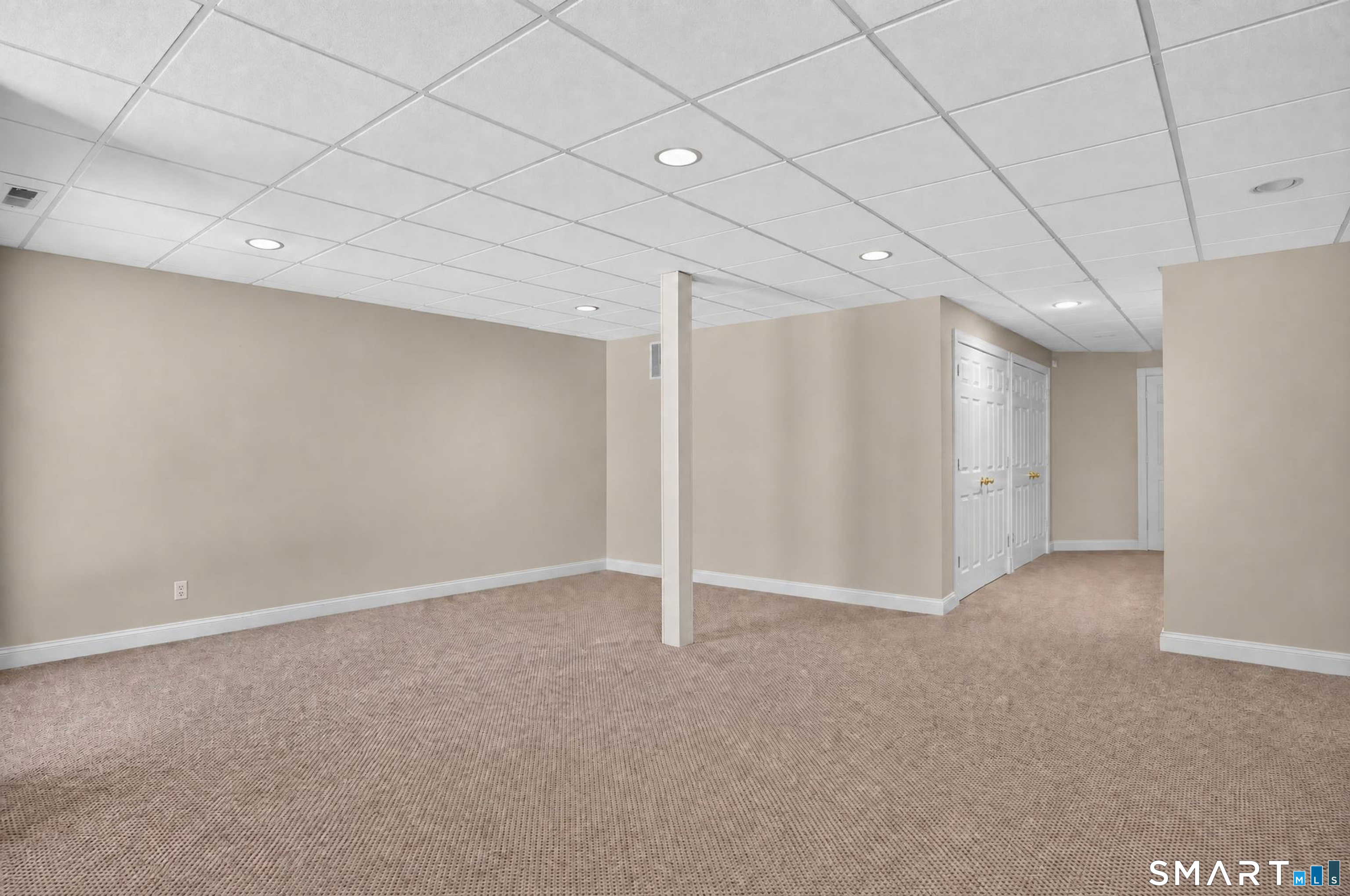 Empty carpeted room with a suspended ceiling, support post, and white double closet doors.