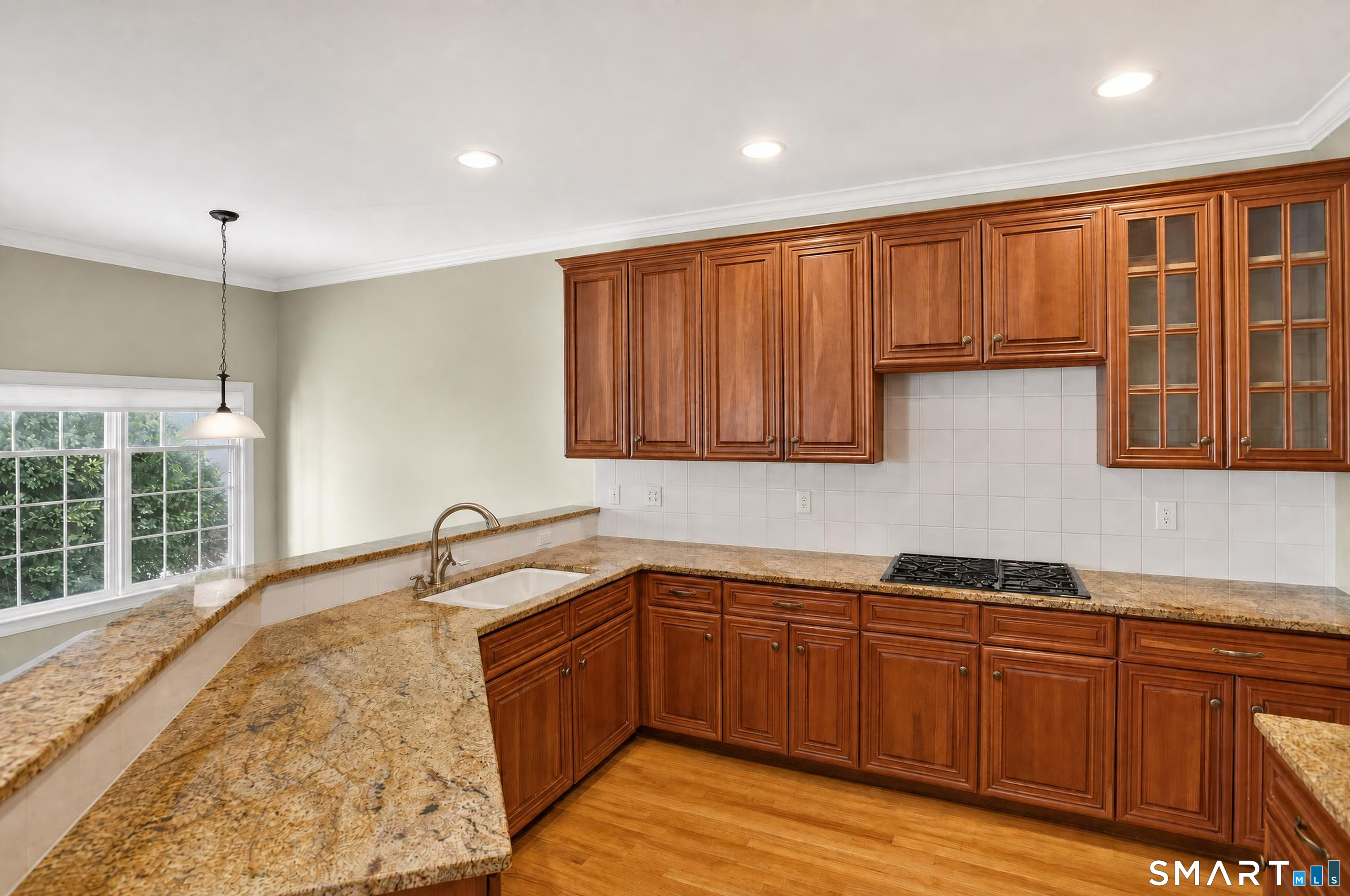 Kitchen with rich wood cabinets, granite counters, a gas cooktop, and a window above the sink.
