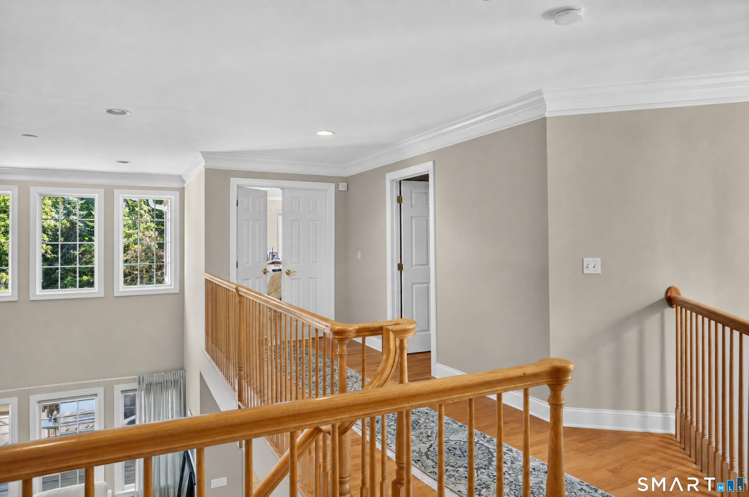 Upstairs landing overlooking the foyer, with wood railings, hardwood floors, and tall windows.
