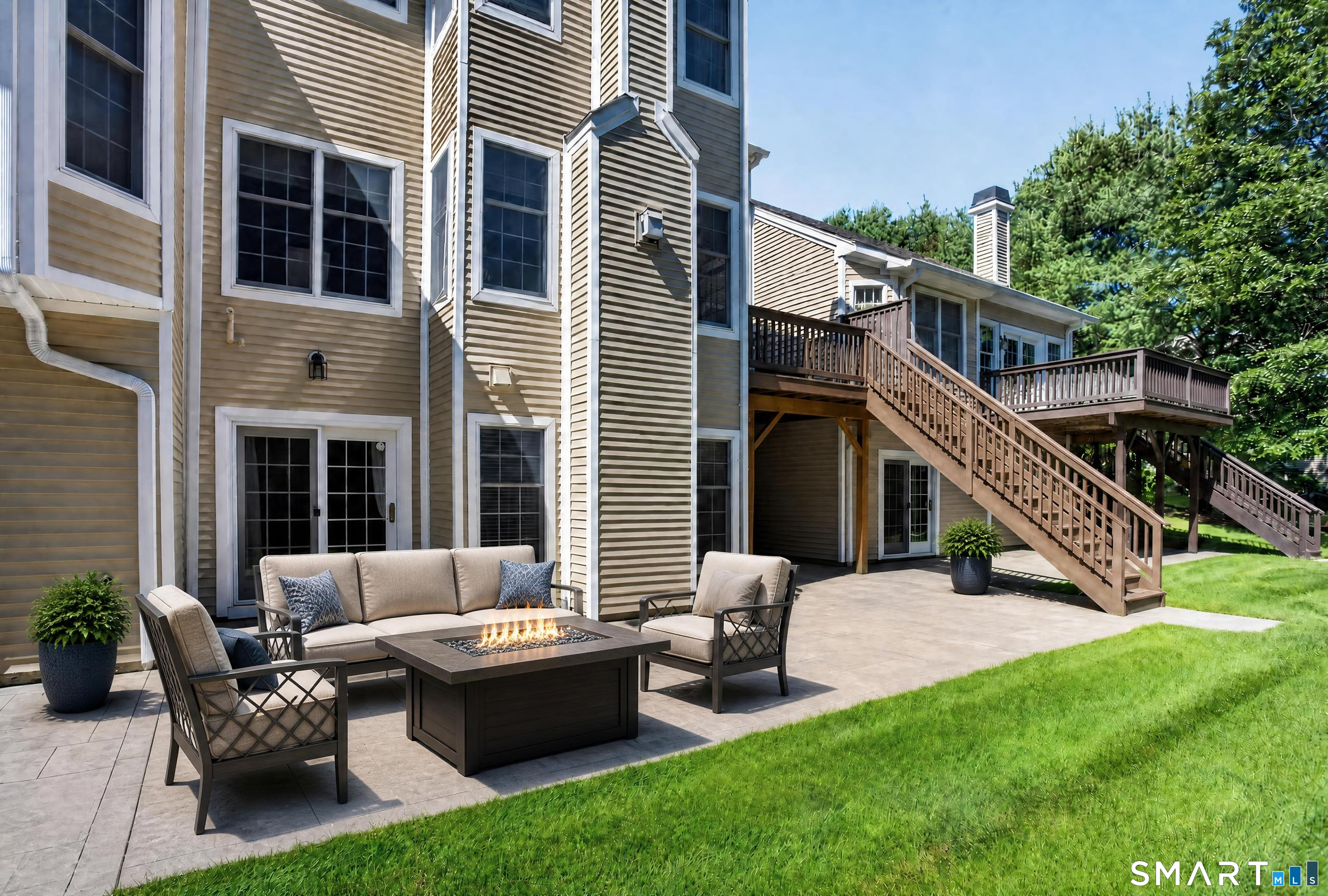 Home’s backyard patio with cushioned seating, a fire table, and stairs leading to elevated wooden decks.