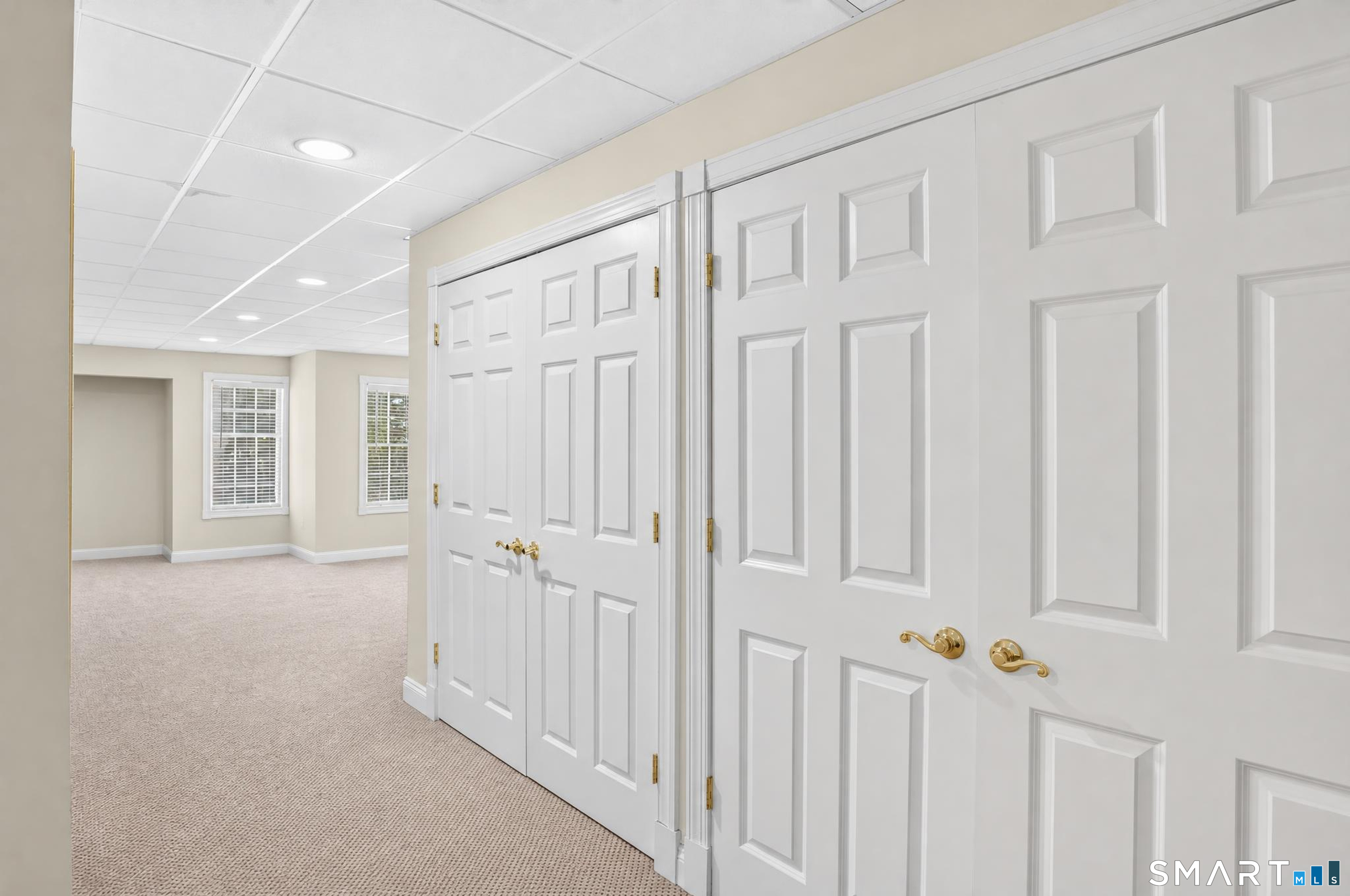Empty carpeted room with windows and a wall of white paneled doors.
