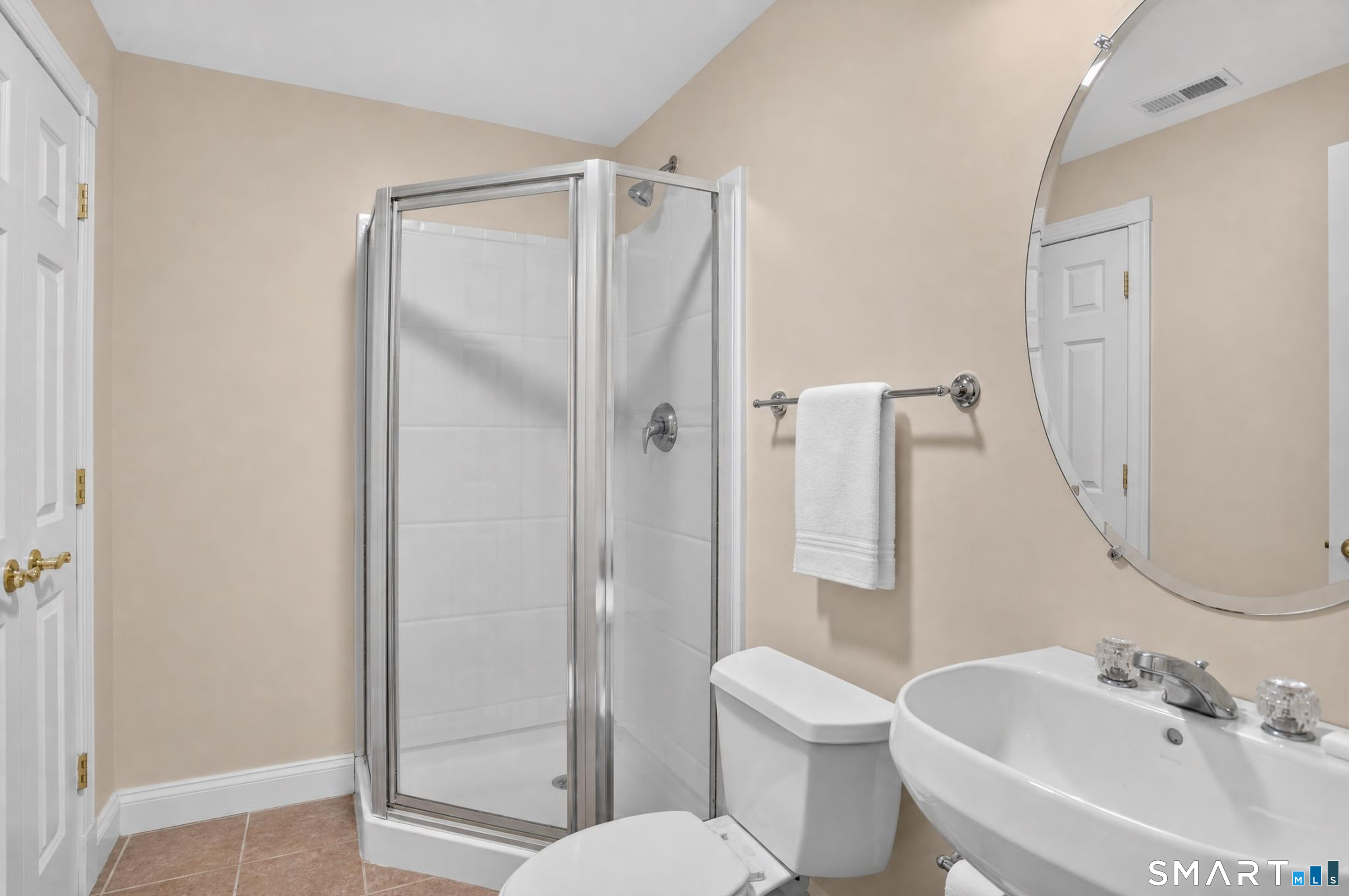 Bathroom with a glass-enclosed shower, white sink, and large round mirror.