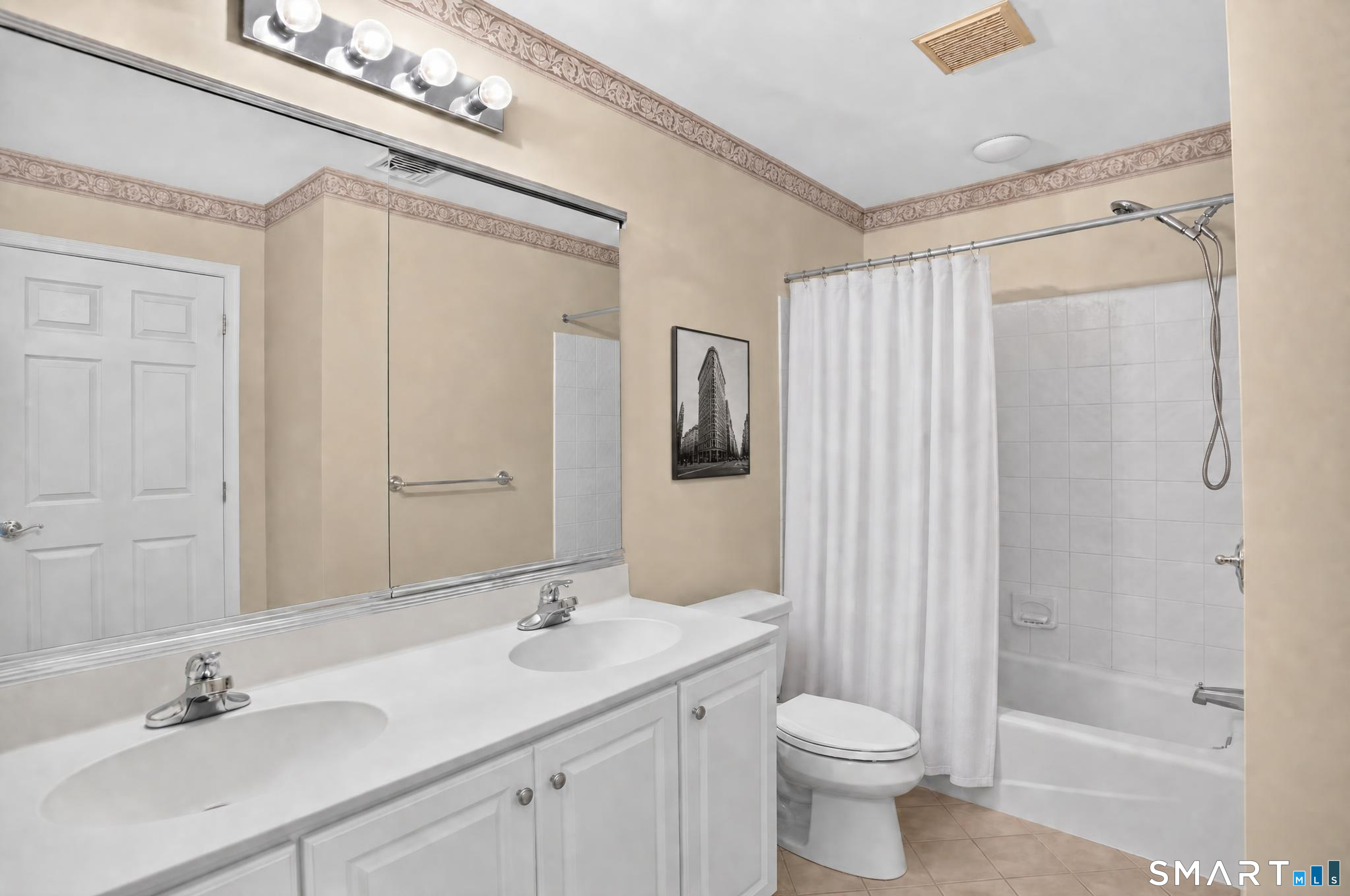 Bathroom with a double-sink vanity, large mirror, and tub-shower behind a white curtain.