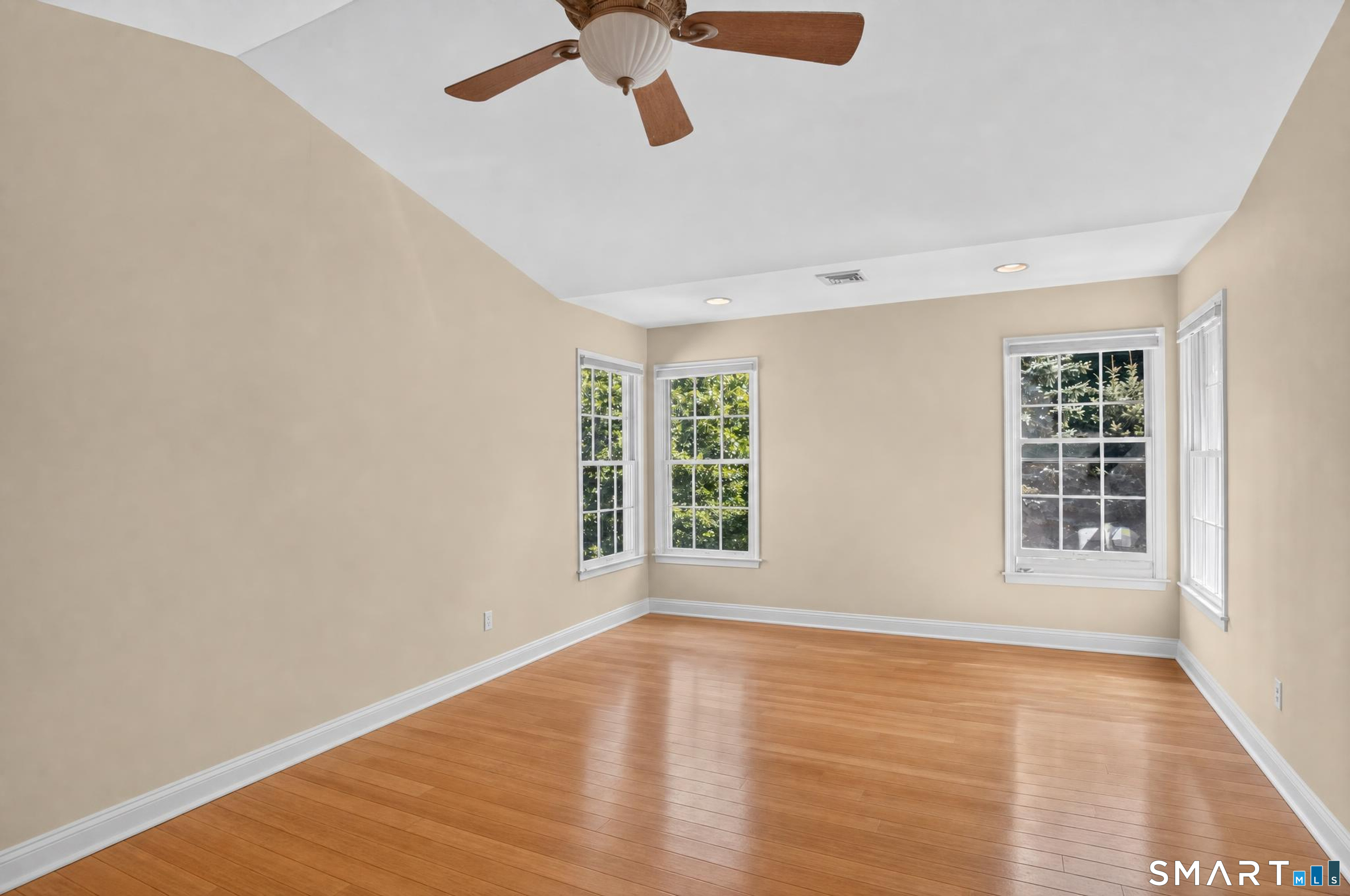 Empty room with hardwood floors, a ceiling fan, and four windows.