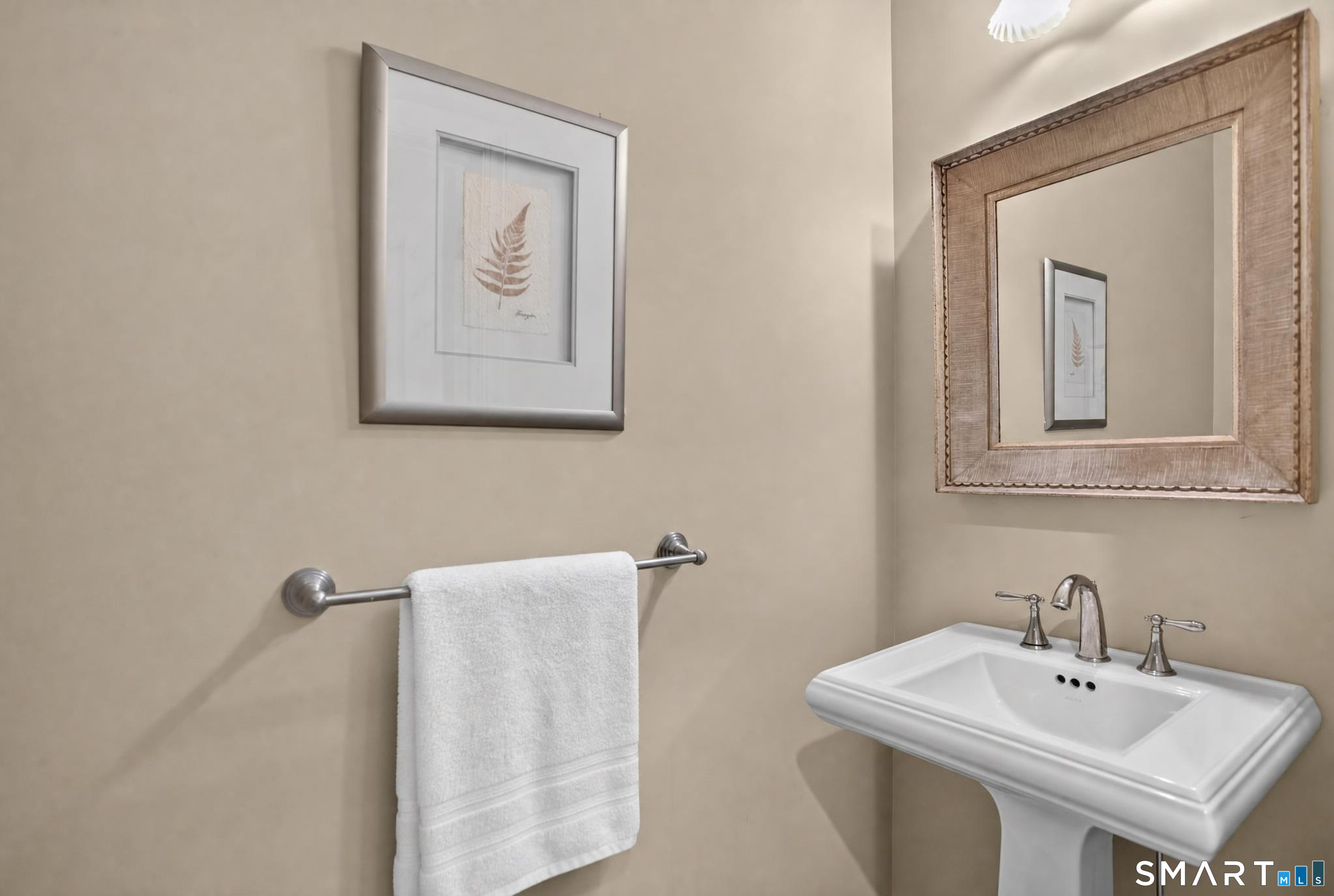 Bathroom pedestal sink with chrome faucets, a white towel, and framed botanical art.