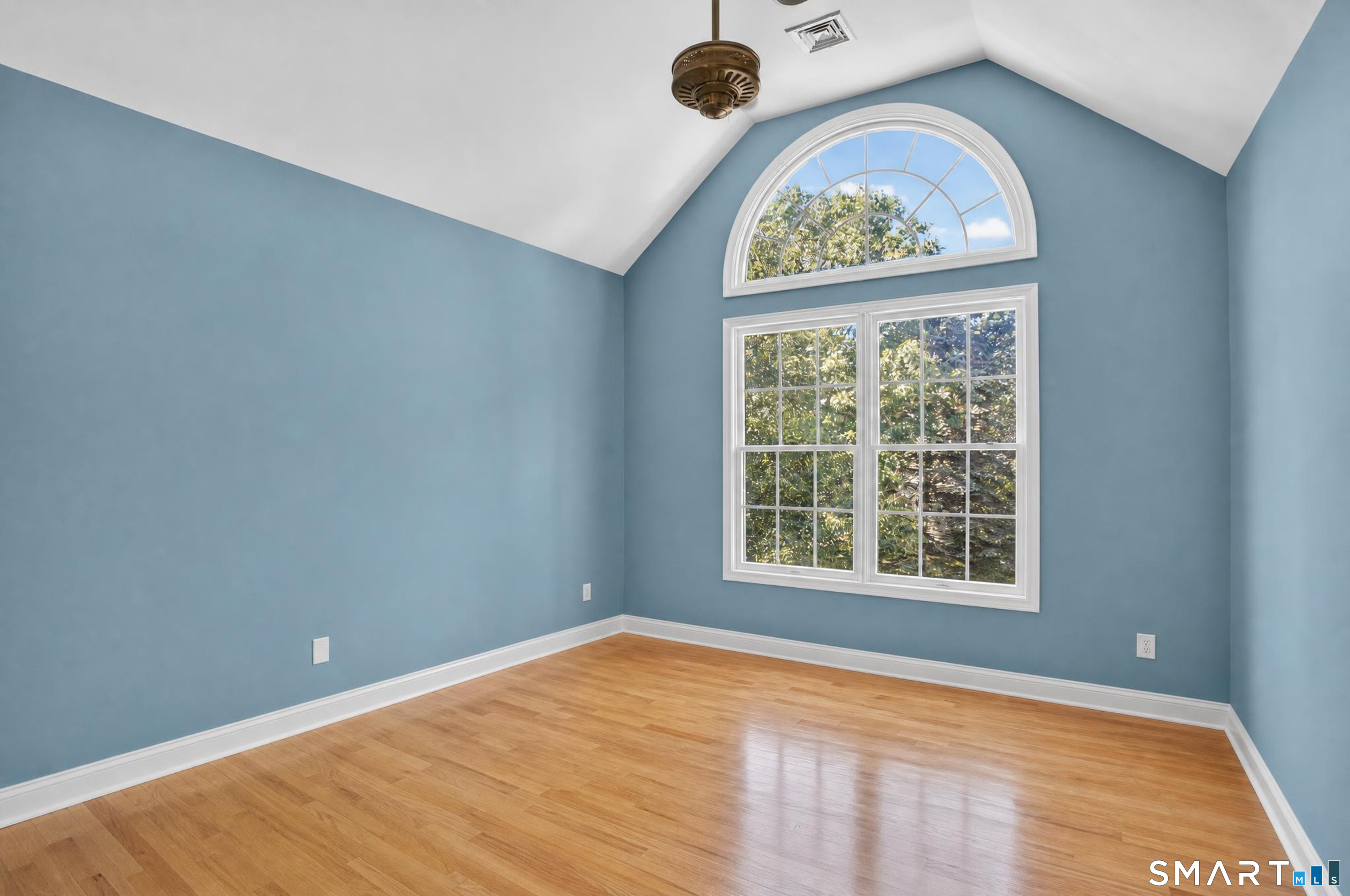 Empty blue room with hardwood floors, vaulted ceiling, and a large arched window.