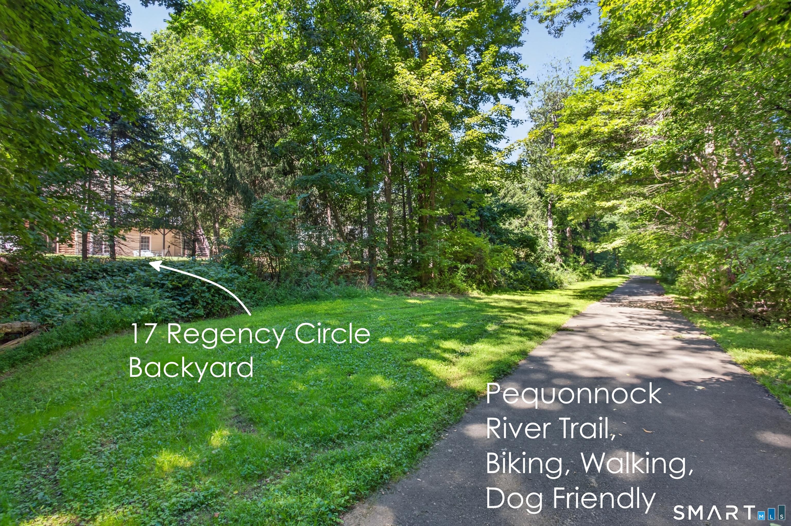 Wooded backyard beside the paved Pequonnock River Trail, with a grassy lawn and mature trees.