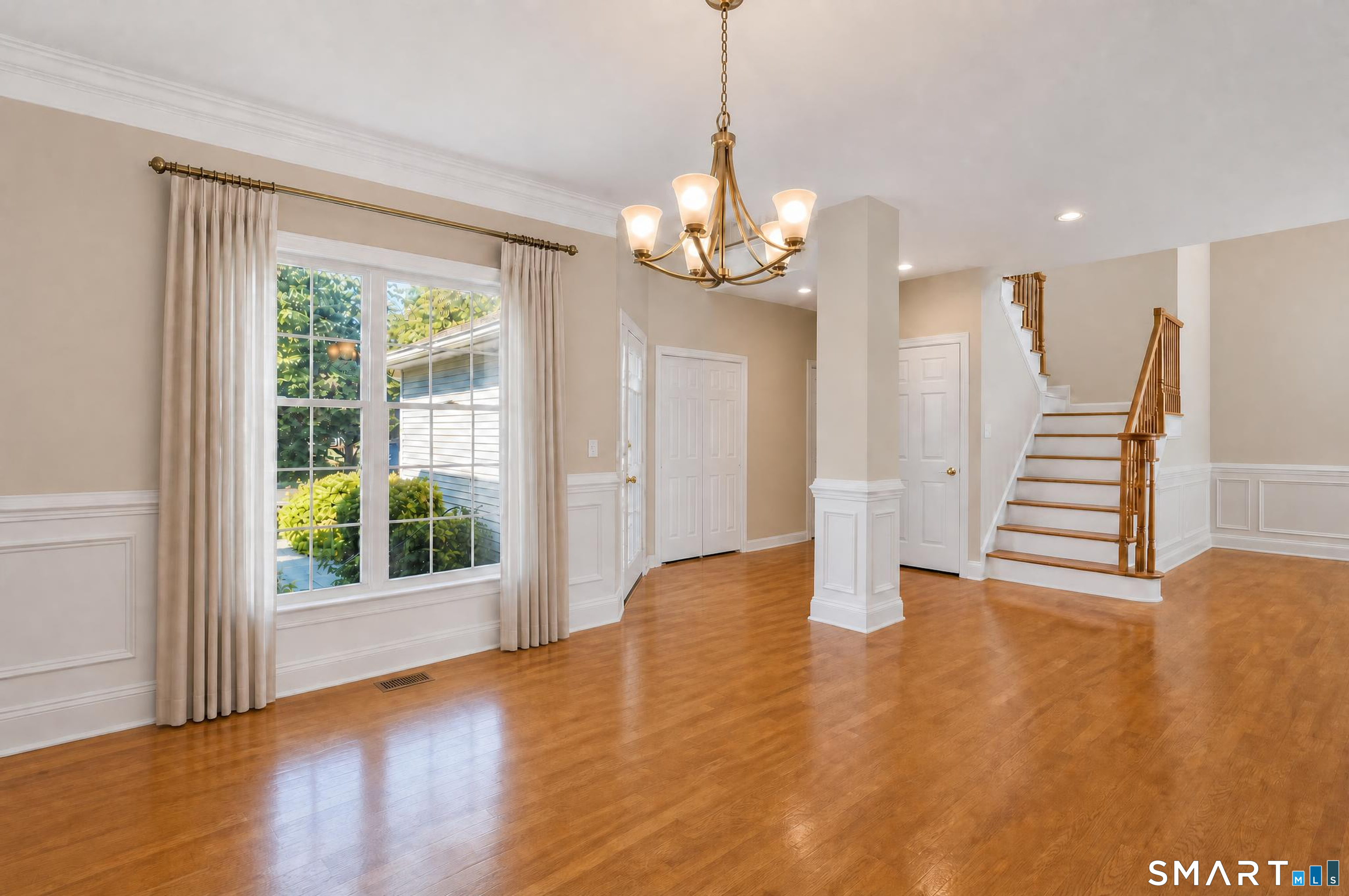 Unfurnished entry hall with polished hardwood floors, a large window, and a staircase with wood railings.