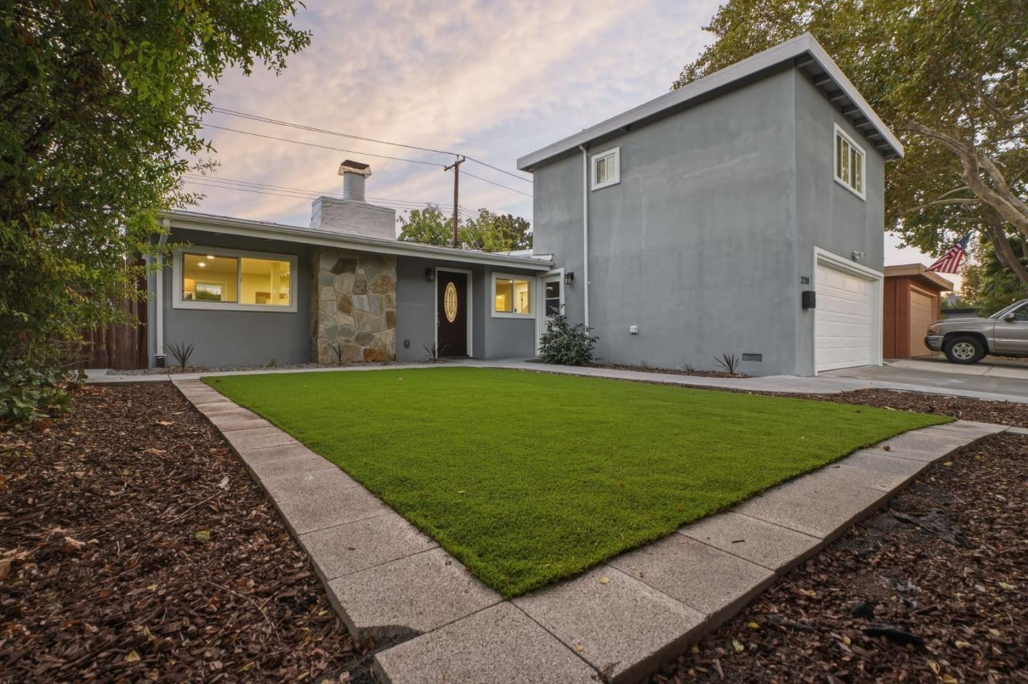 Gray two-story house with a stone chimney, attached garage, and neatly edged front lawn.