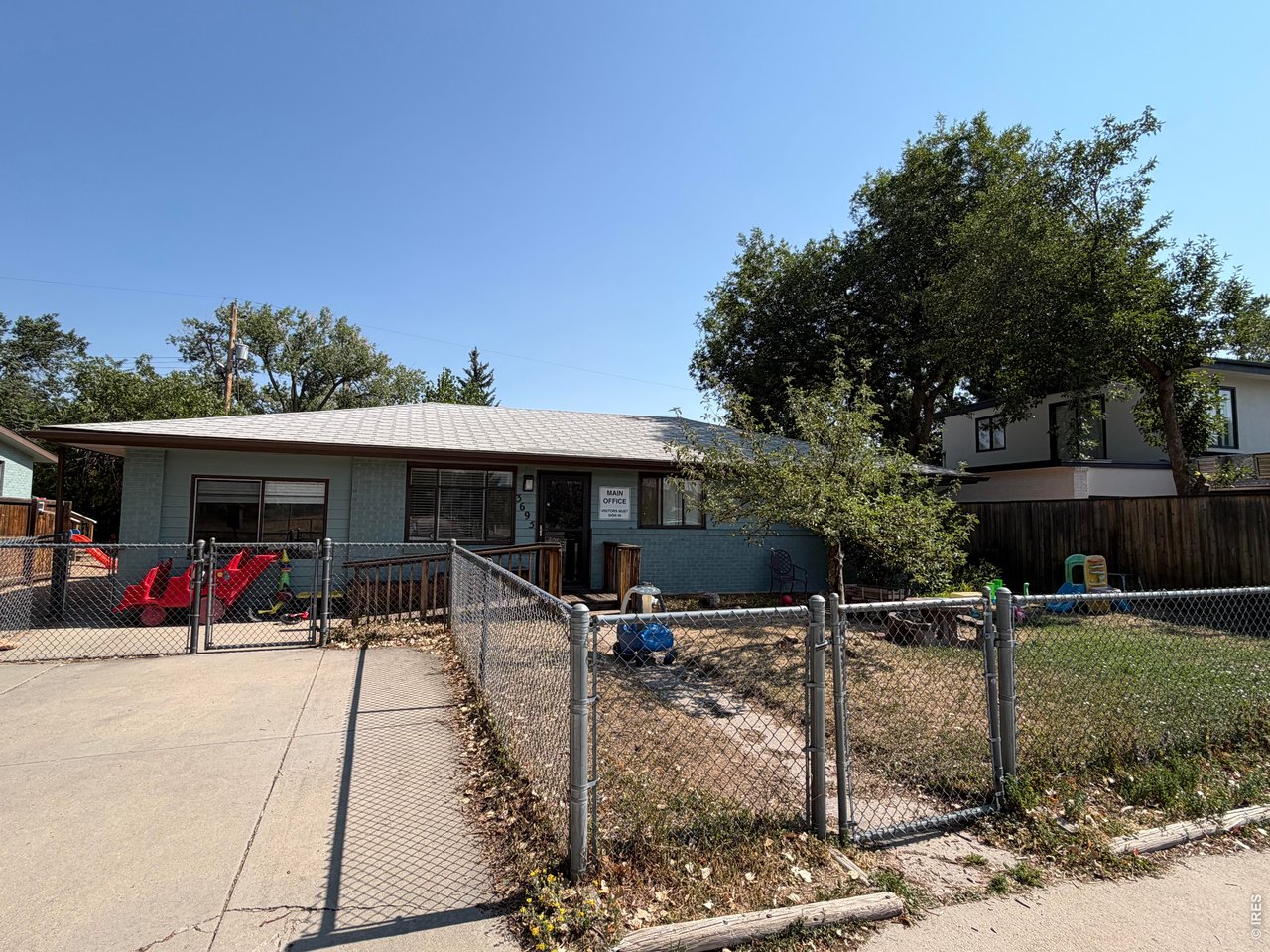 Single-story blue-brick building with a fenced yard, playground toys, and a MAIN OFFICE sign.