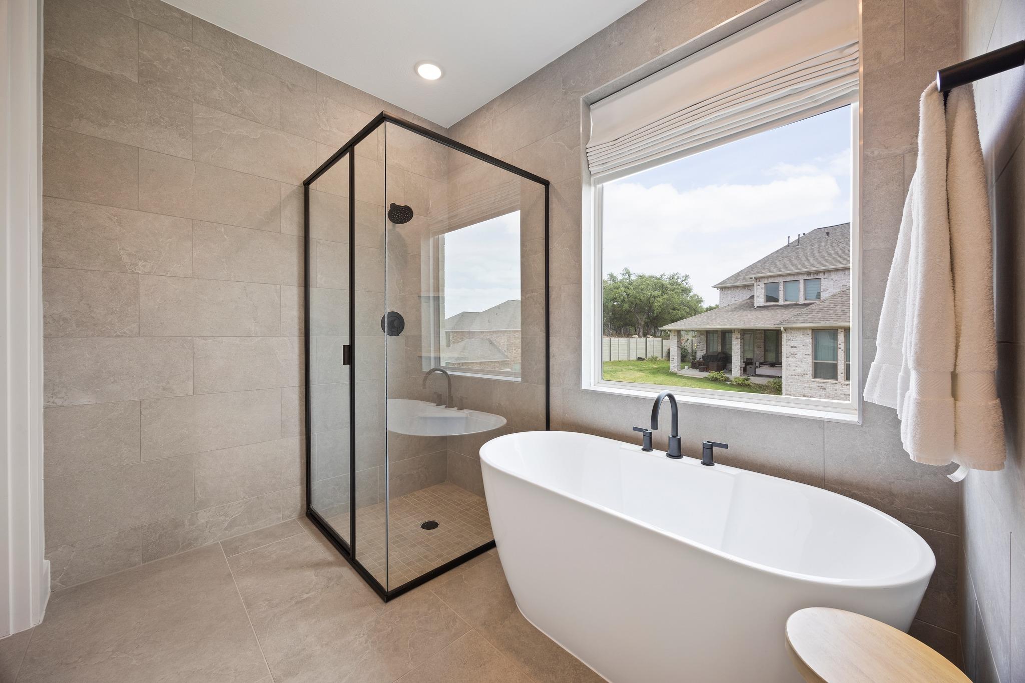 Bathroom with a freestanding soaking tub and black-framed glass shower beside a large window.