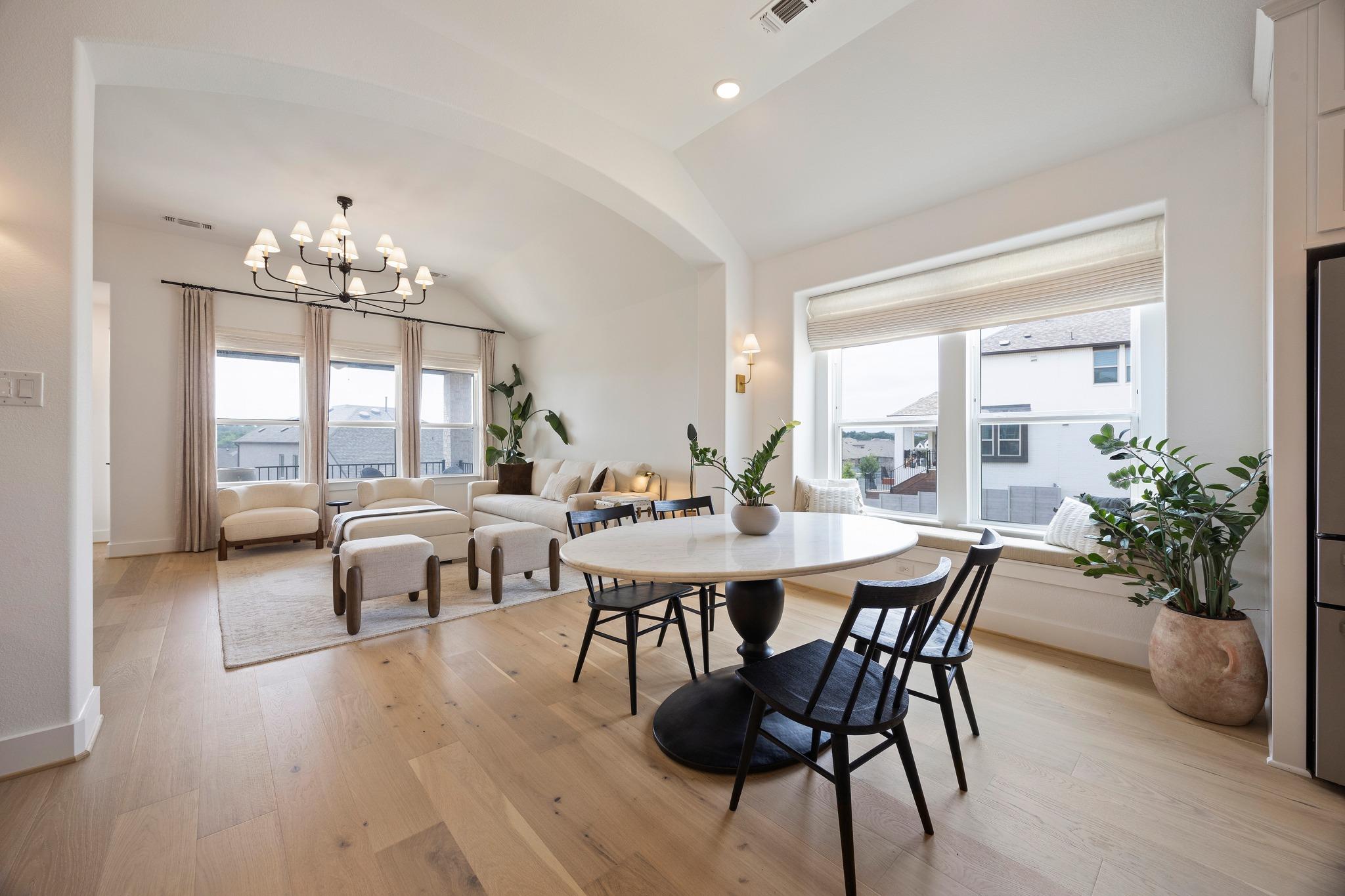Open living and dining room with vaulted ceilings, large windows, and light hardwood floors.