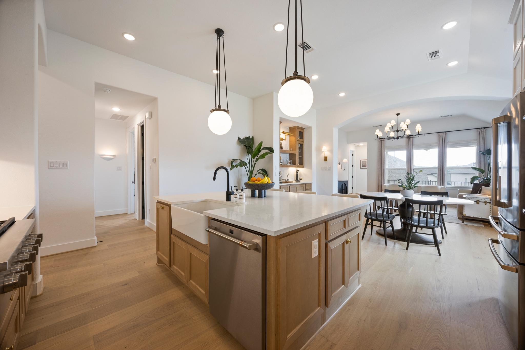 Open kitchen with a large white island, warm wood cabinets, and an adjoining dining area.