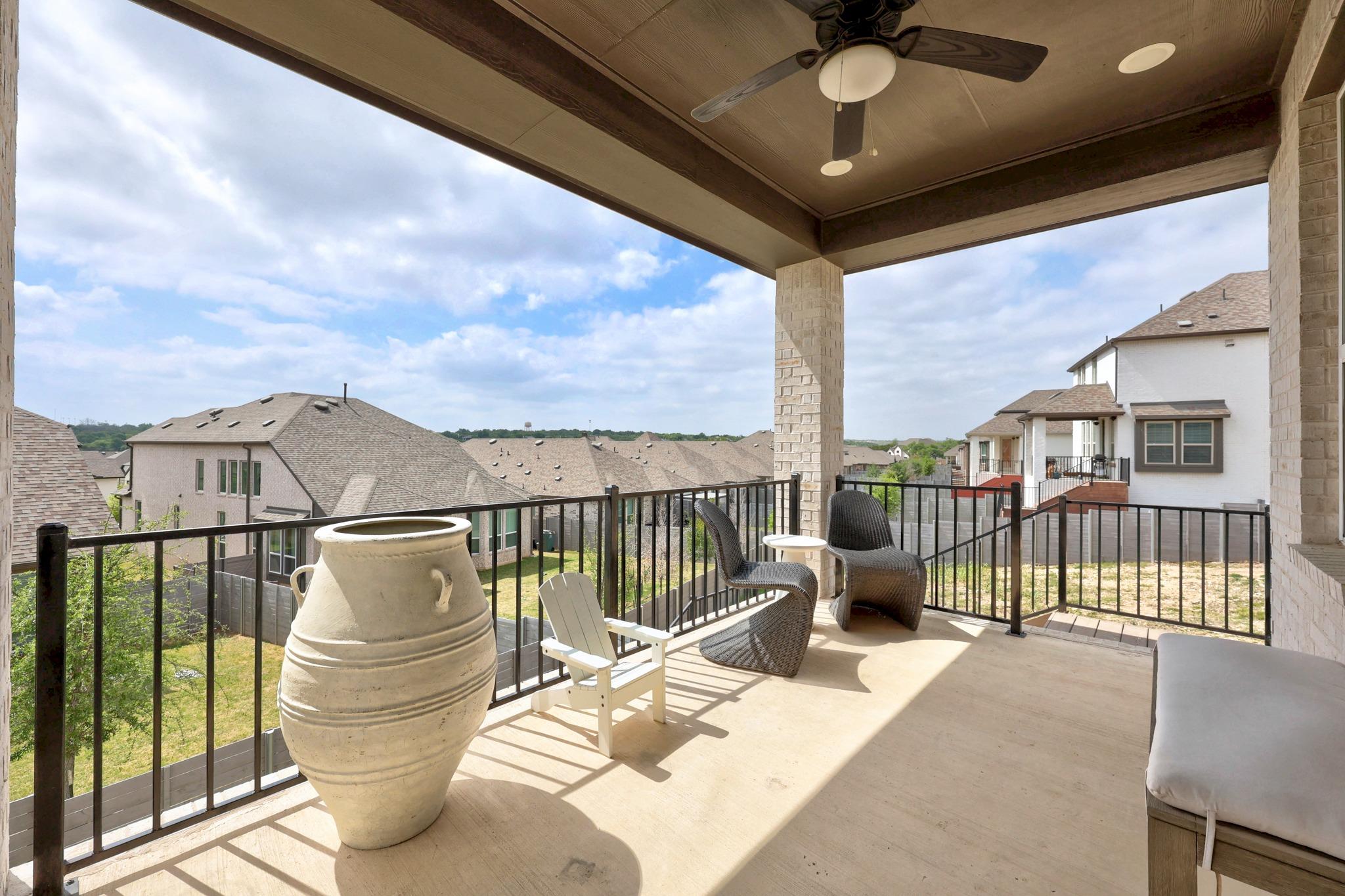 Covered patio with wicker seating and a large ceramic planter overlooking nearby homes.