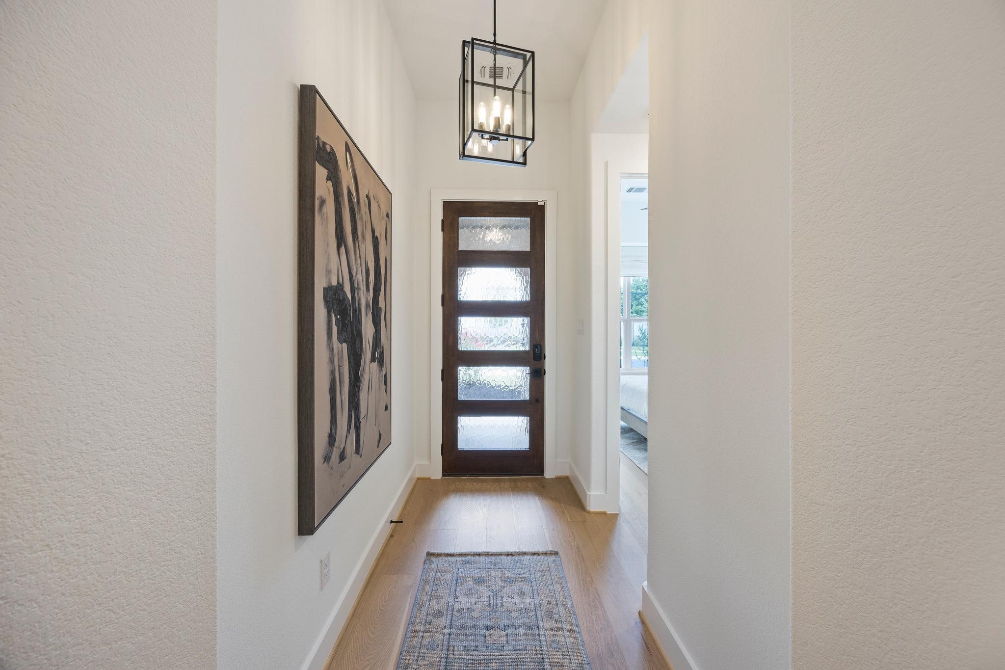 Entry foyer with a dark wood glass-paneled front door, geometric pendant, and patterned runner.