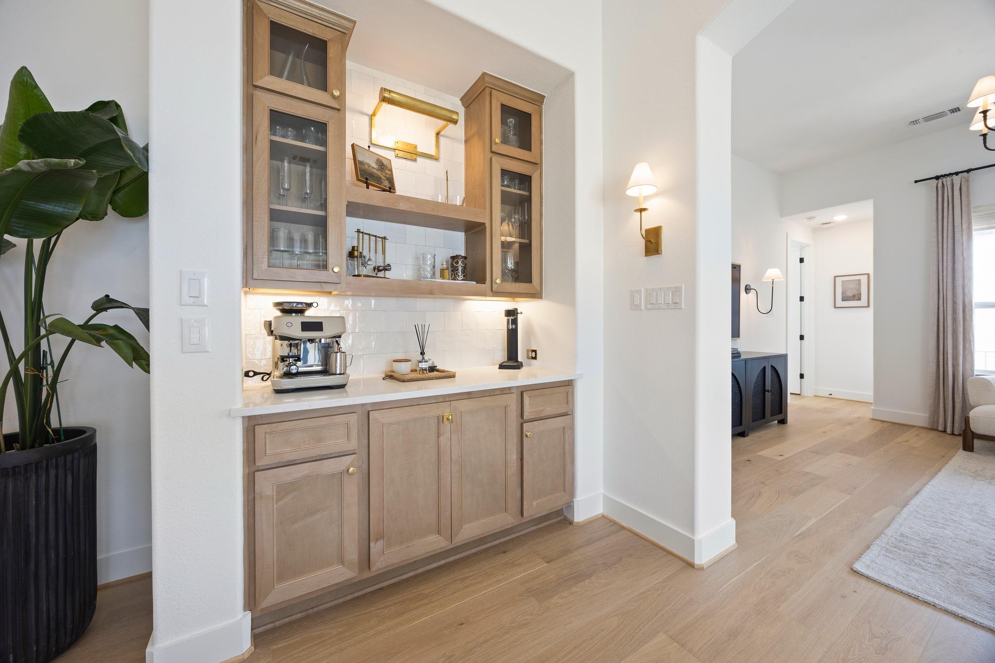 Built-in wood wet bar with glass-front cabinets and a coffee machine beside the living area