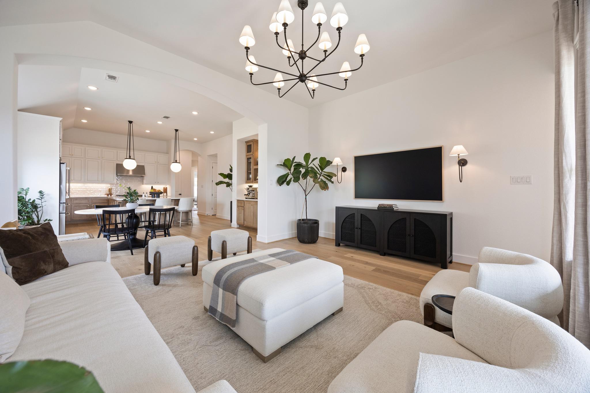 Open-plan living room with white seating, a black media console, and kitchen and dining area beyond.