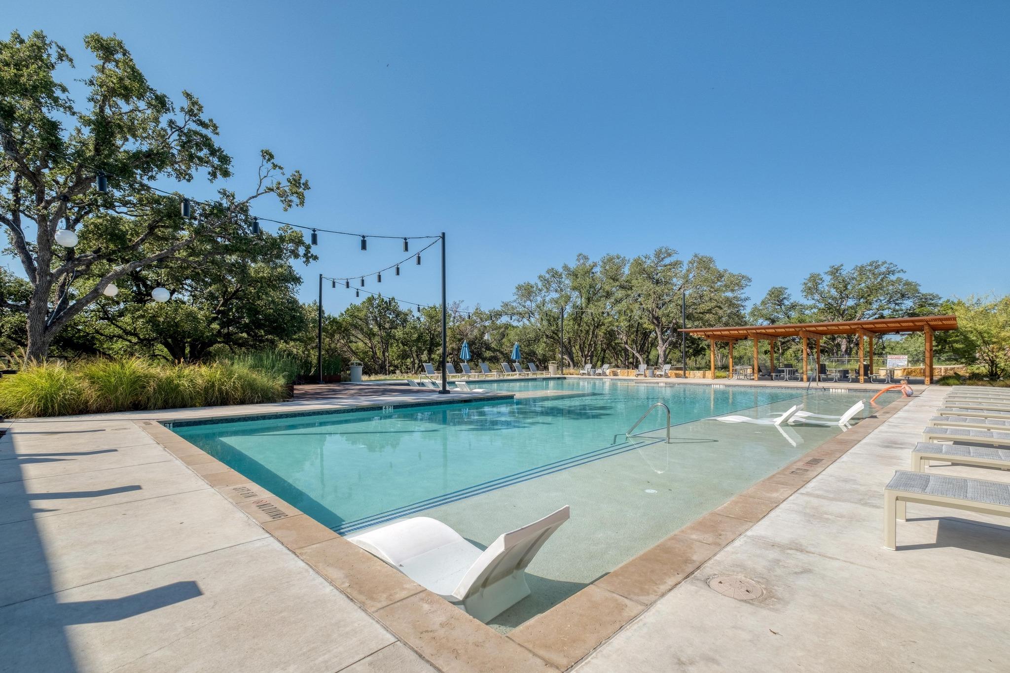 Outdoor swimming pool with a shallow tanning ledge, in-water loungers, string lights, and a wooden pavilion.
