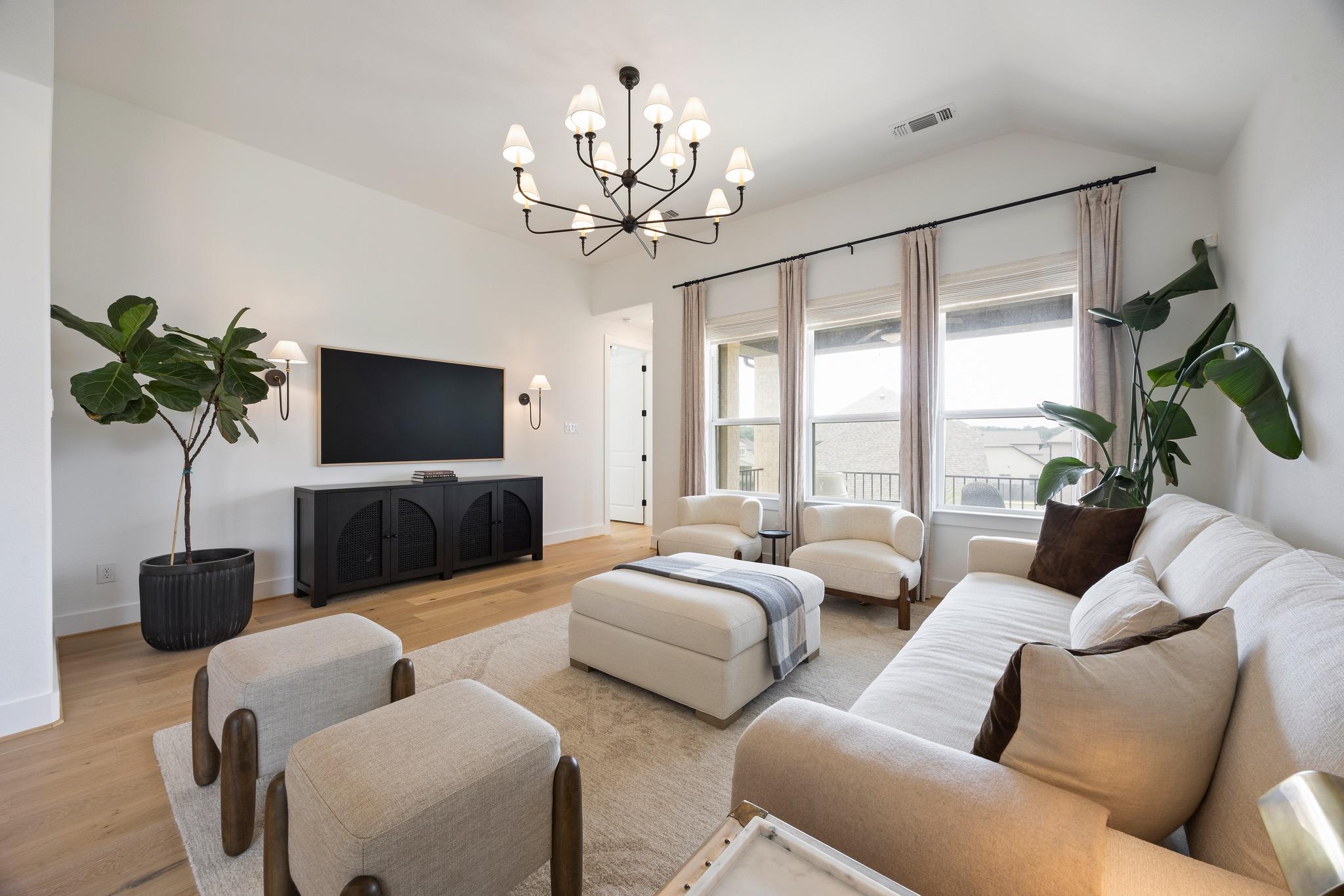 Staged living room with a white sectional, tall curtained windows, and a black chandelier.