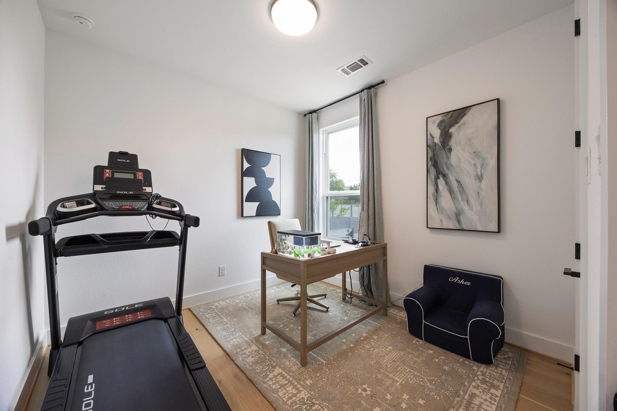 Home office and exercise room with a treadmill, wooden desk, aquarium, and dark armchair.