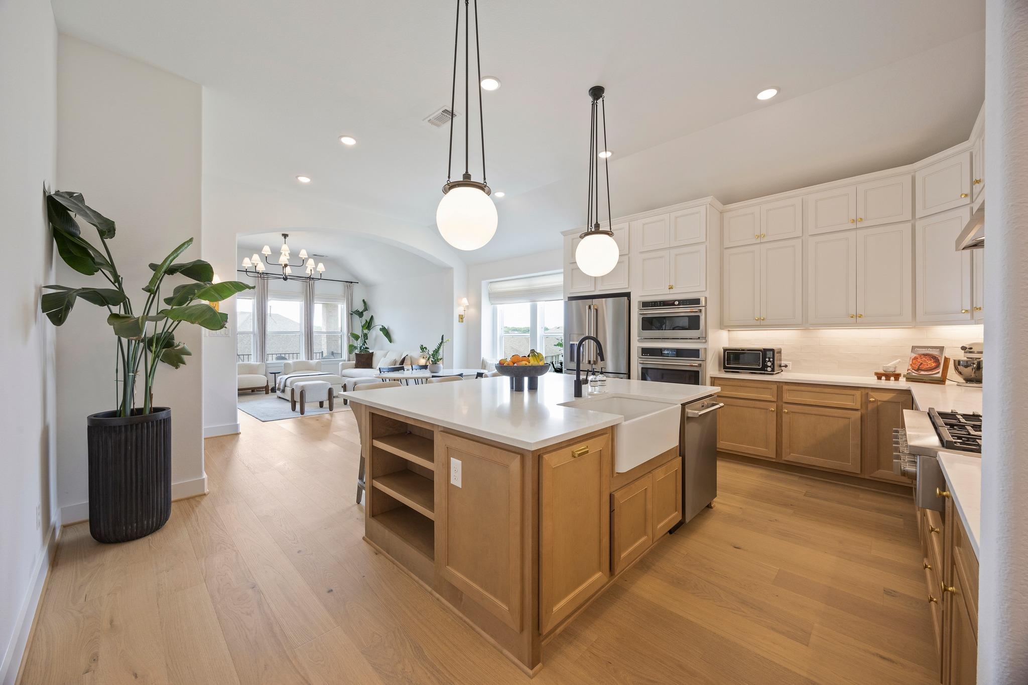 Open kitchen with a large white island, farmhouse sink, pendant lights, and adjoining furnished living area.