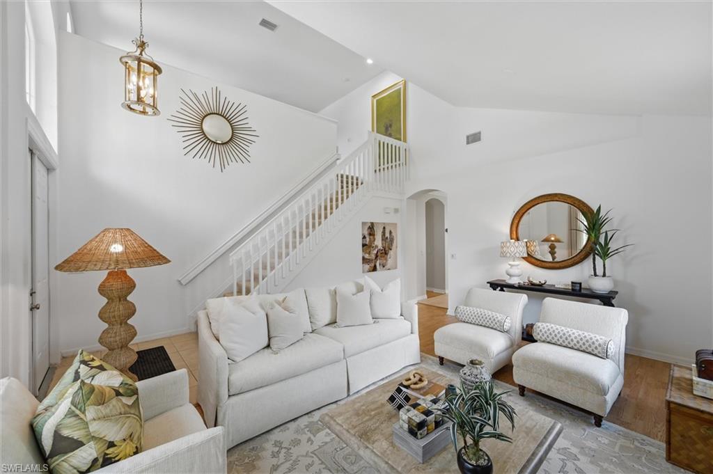 Staged living room with white seating, a staircase, and high ceilings.