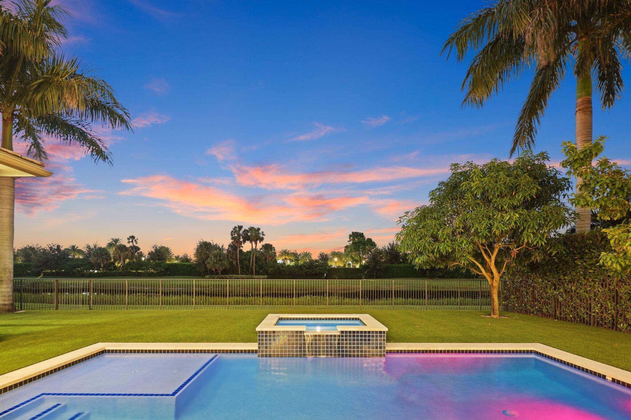 Backyard pool and raised spa at dusk, framed by palm trees beneath a pink sunset sky.