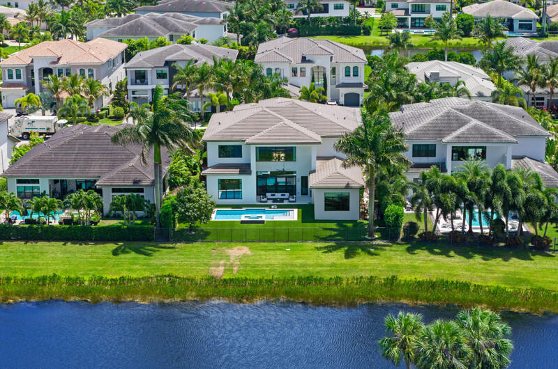 Aerial view of a modern waterfront home with a backyard pool and palm-lined lawn.