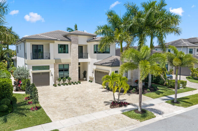 Two-story modern home with stone driveway, balconies, and palm trees in front.