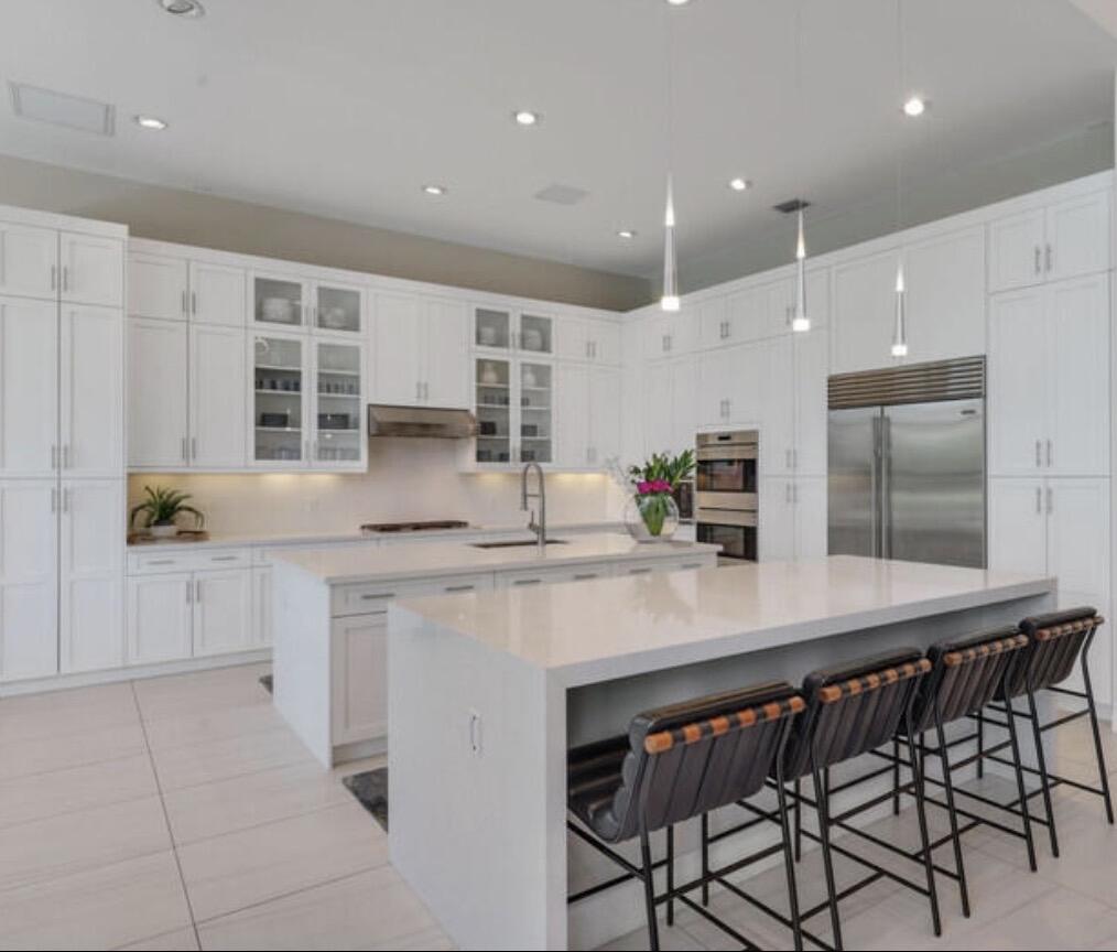 Bright white kitchen with oversized island, dark bar stools, and stainless-steel appliances.