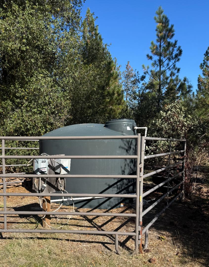 Water storage tank enclosed by a metal rail fence among trees.