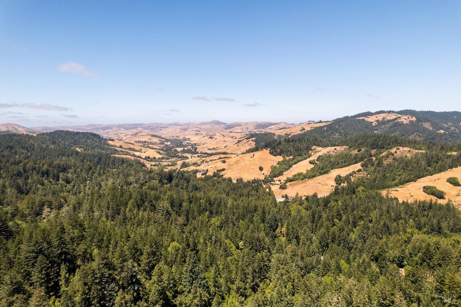 Aerial view of forested hills and golden rolling countryside with a small valley settlement.