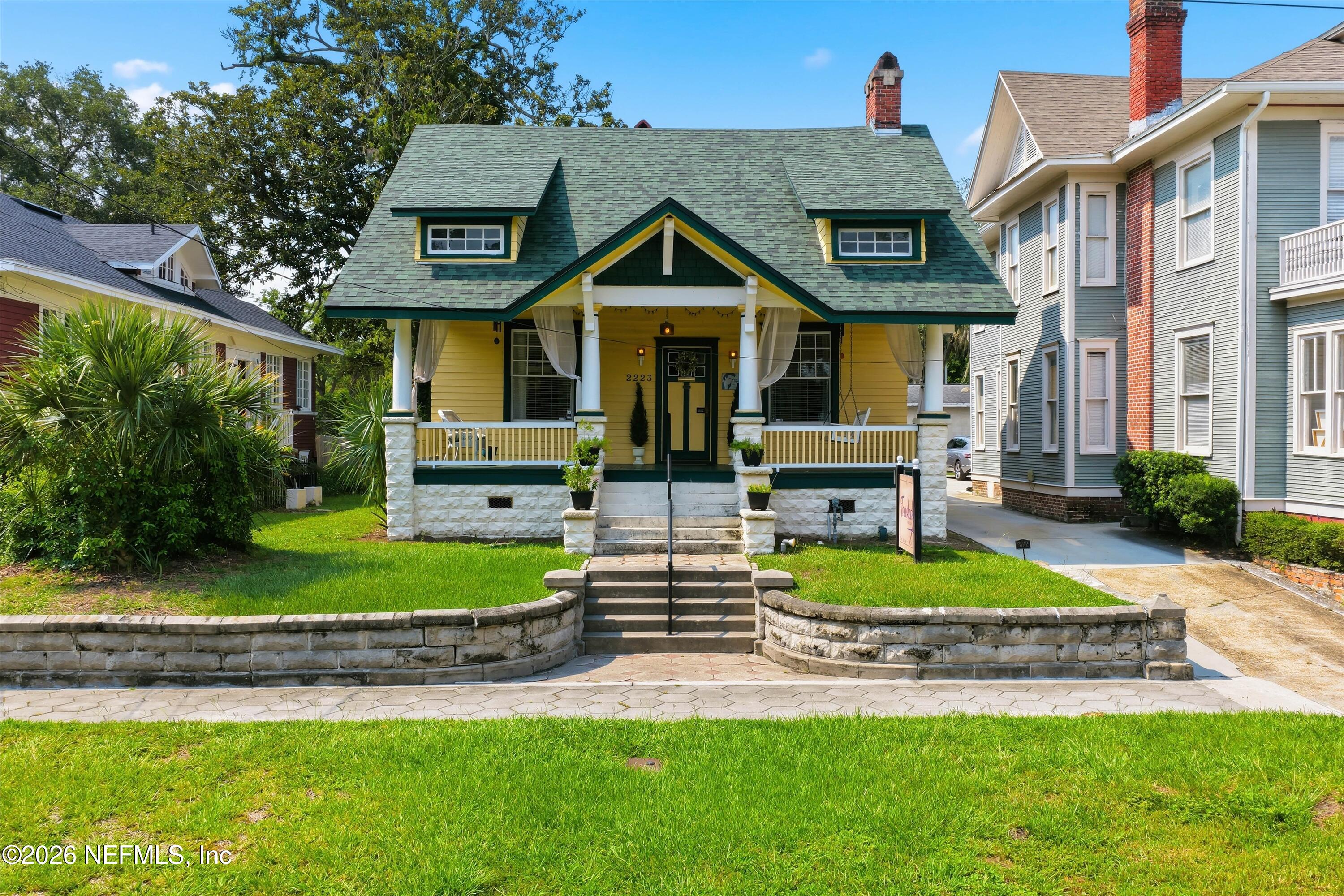Yellow Craftsman house with a green roof, covered porch, and stone front steps.