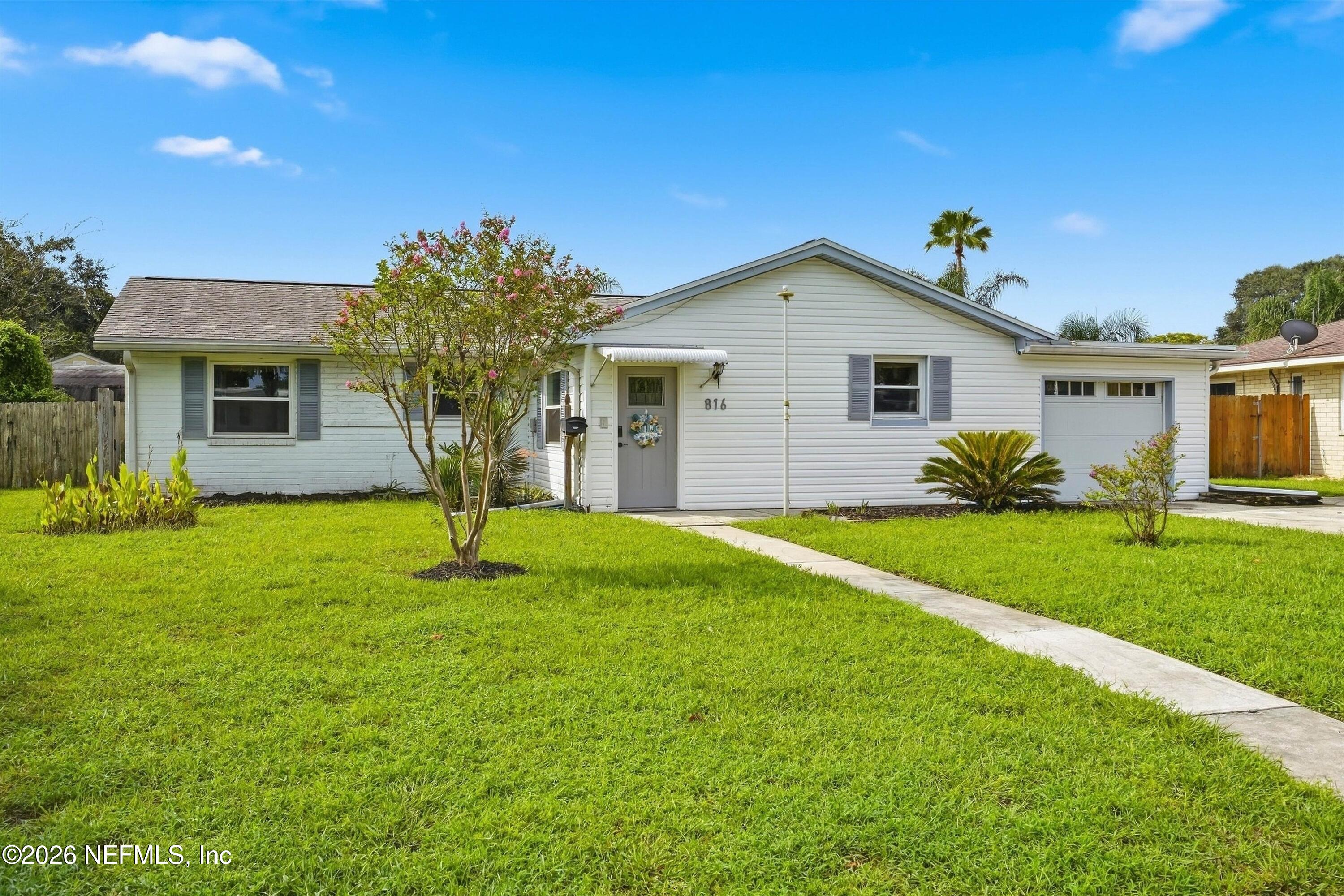 White single-story house with attached garage, green lawn, and flowering tree.