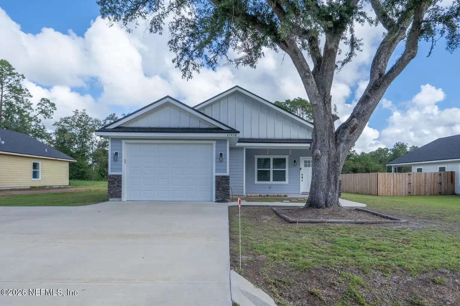 Light blue house with a double garage, wide driveway, and a large oak tree in the front yard.