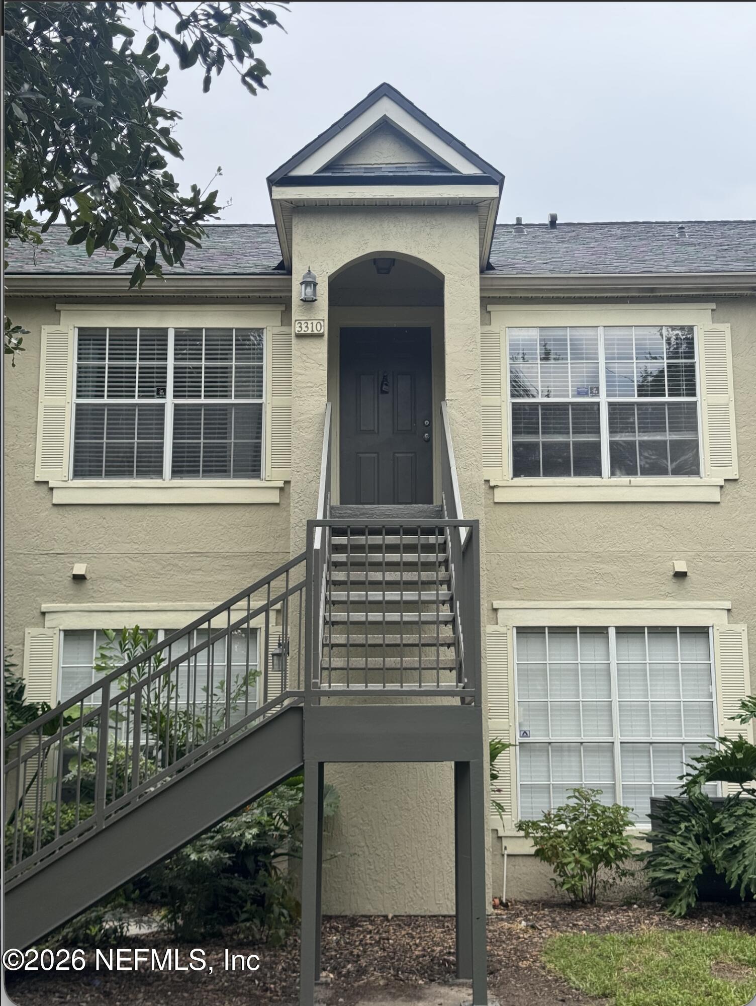 Beige residential building with an elevated entrance, central metal staircase, and shuttered windows.