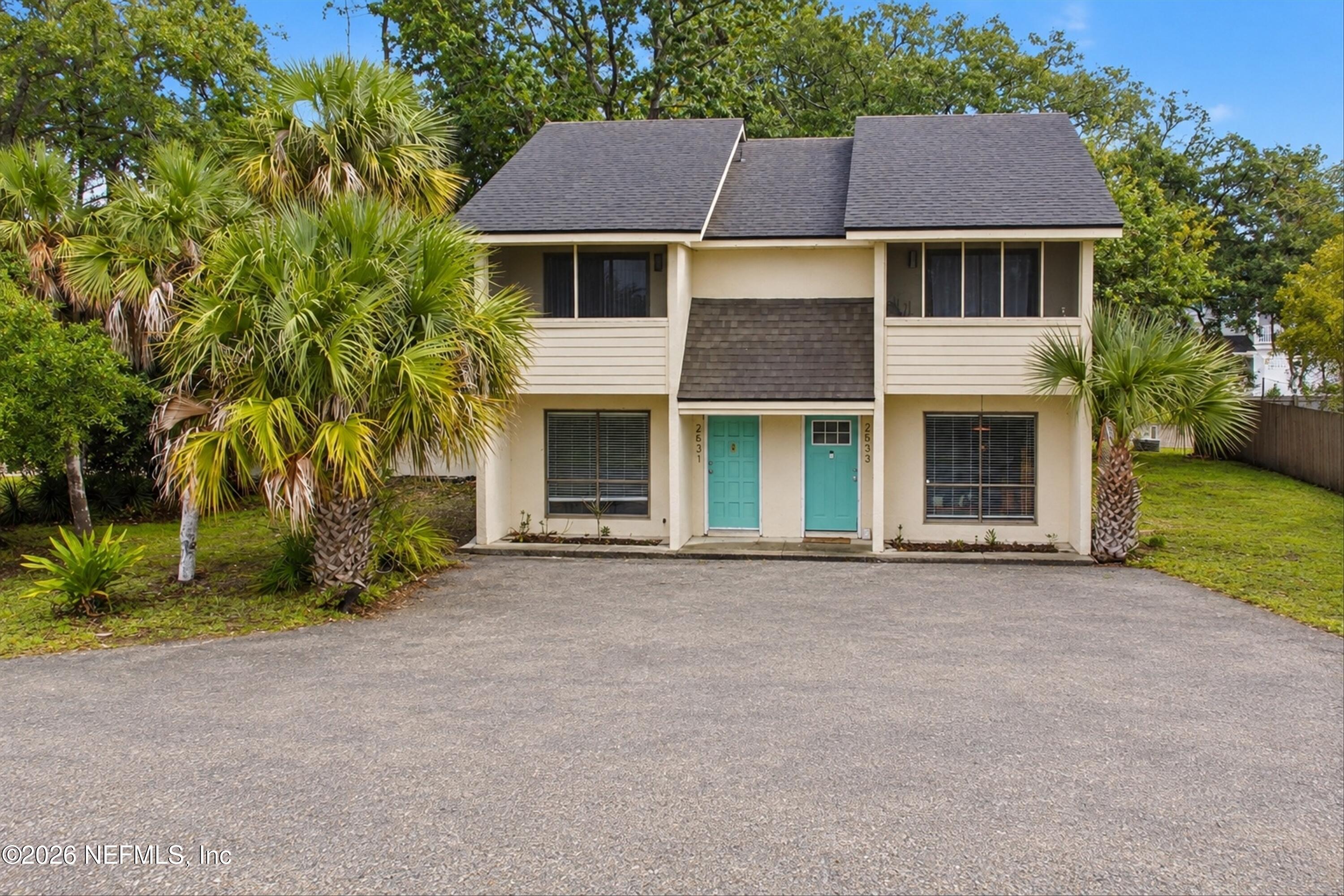 Two-story cream home with turquoise doors, palm trees, and a wide paved driveway.
