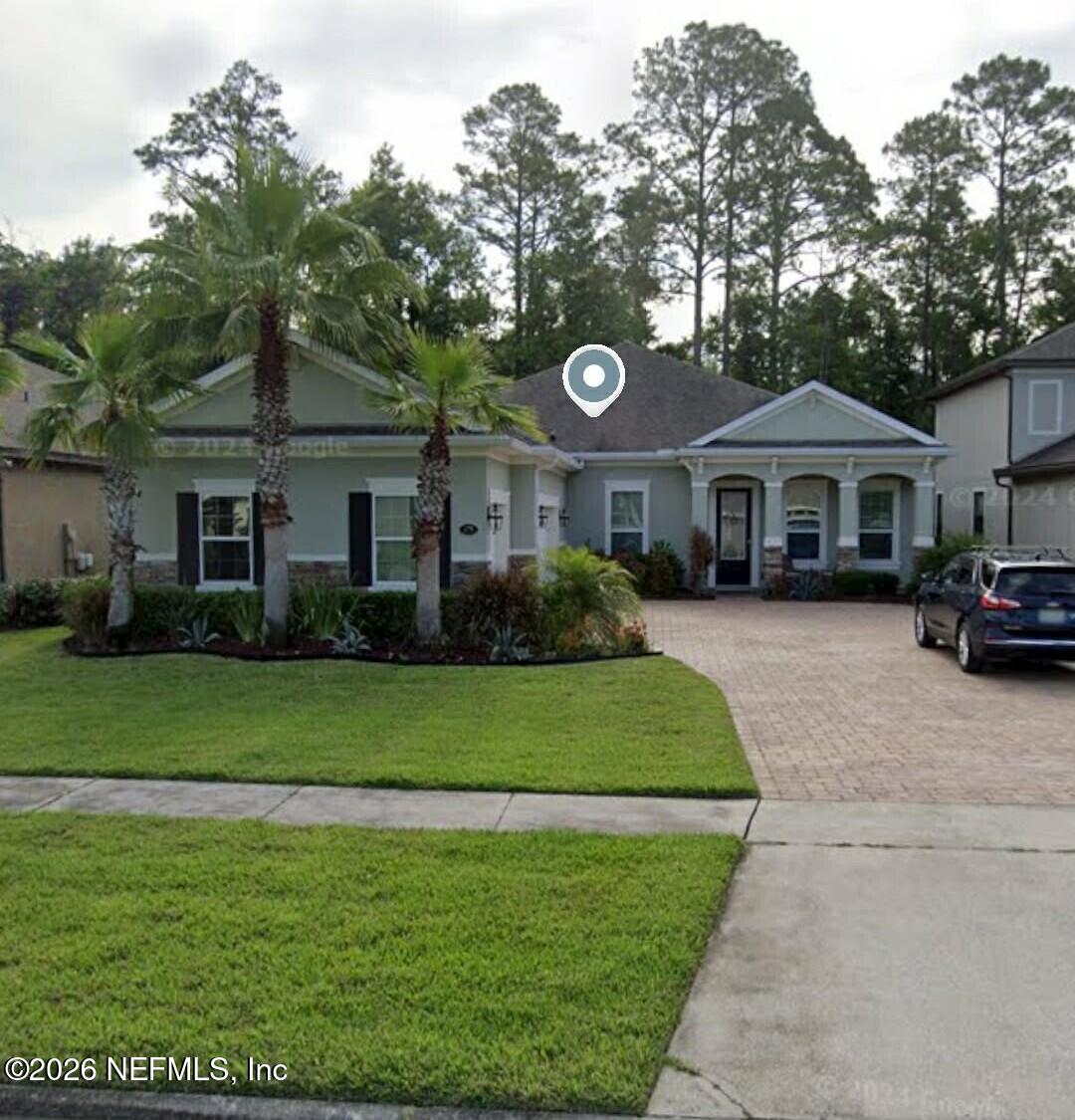 Gray single-story home with a covered porch, palm trees, and a paved driveway.
