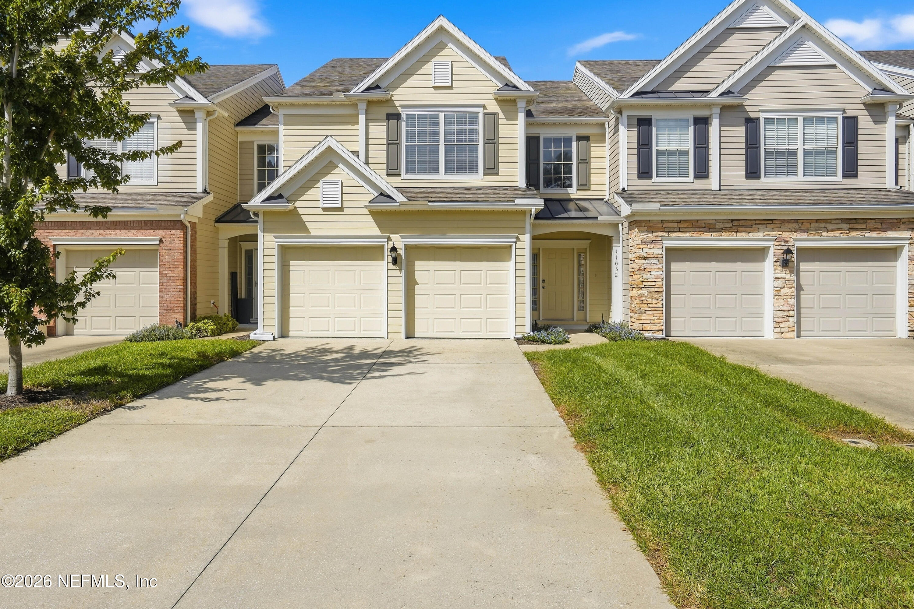Beige two-story townhouse with a double garage, stone accents, and a broad driveway.
