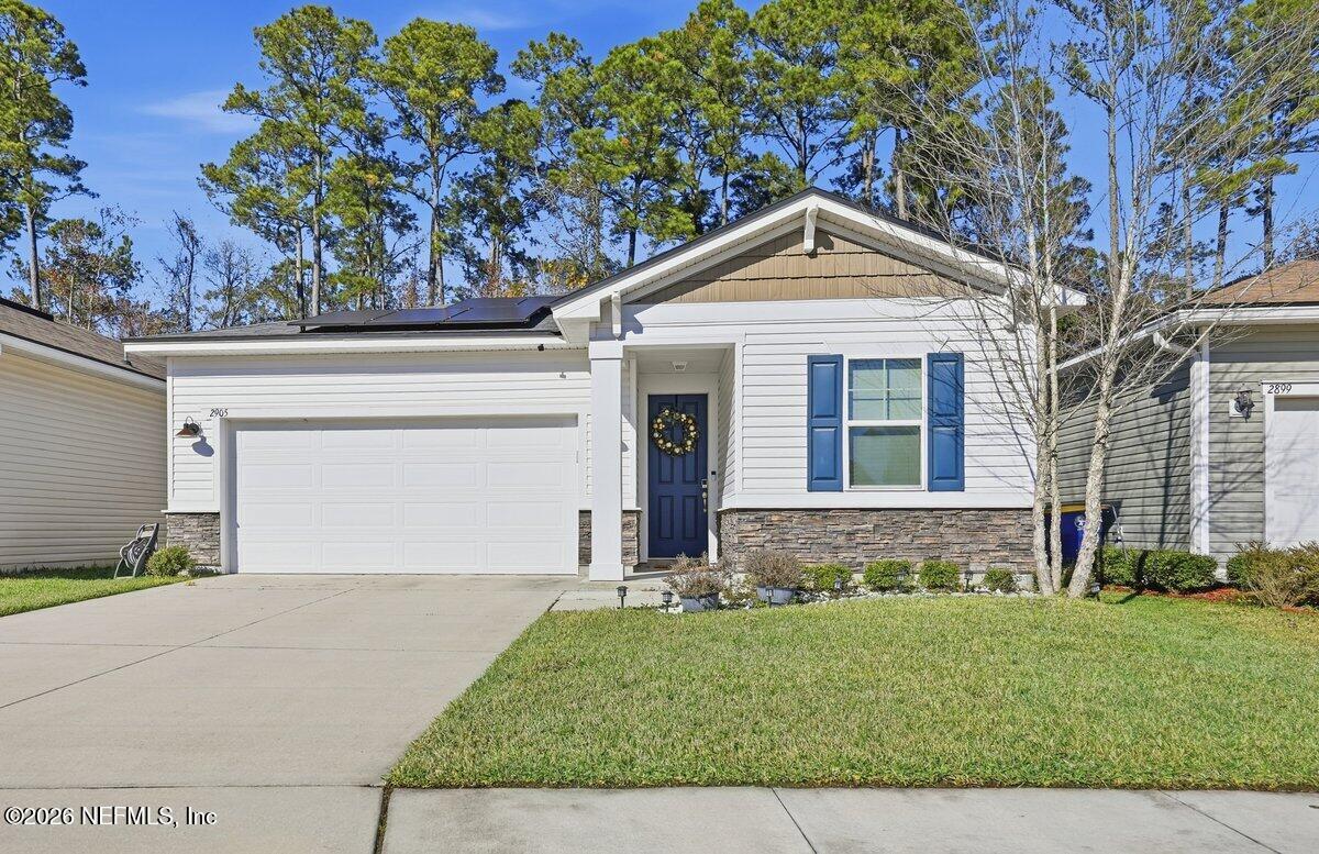 White single-story home with blue shutters, a two-car garage, and solar panels on the roof.