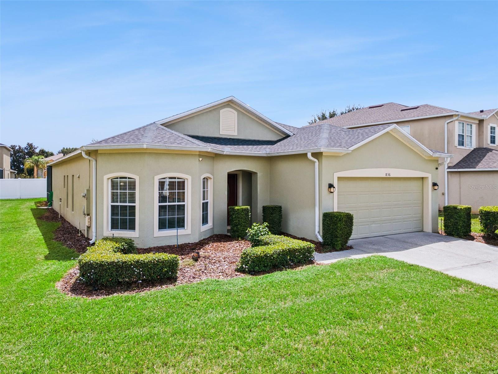 Single-story beige stucco home with a two-car garage, arched windows, and a neatly trimmed lawn.