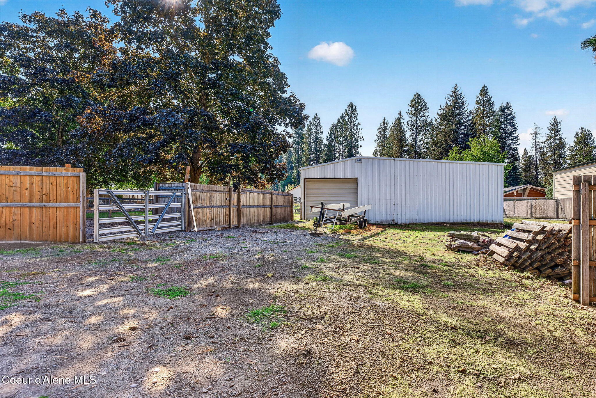 Fenced backyard with a white metal outbuilding, roll-up garage door, and mature trees.