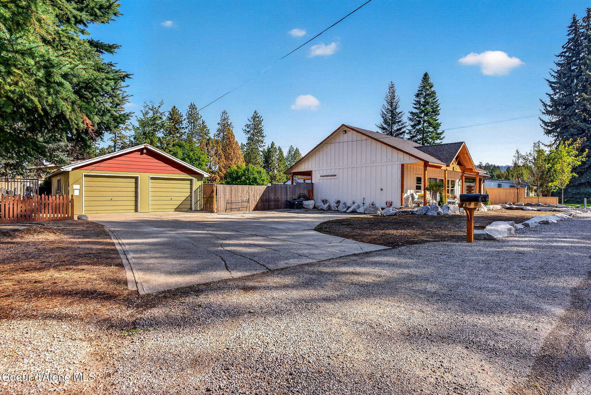 Home with wood-trimmed exterior, detached double garage, and broad gravel parking area.
