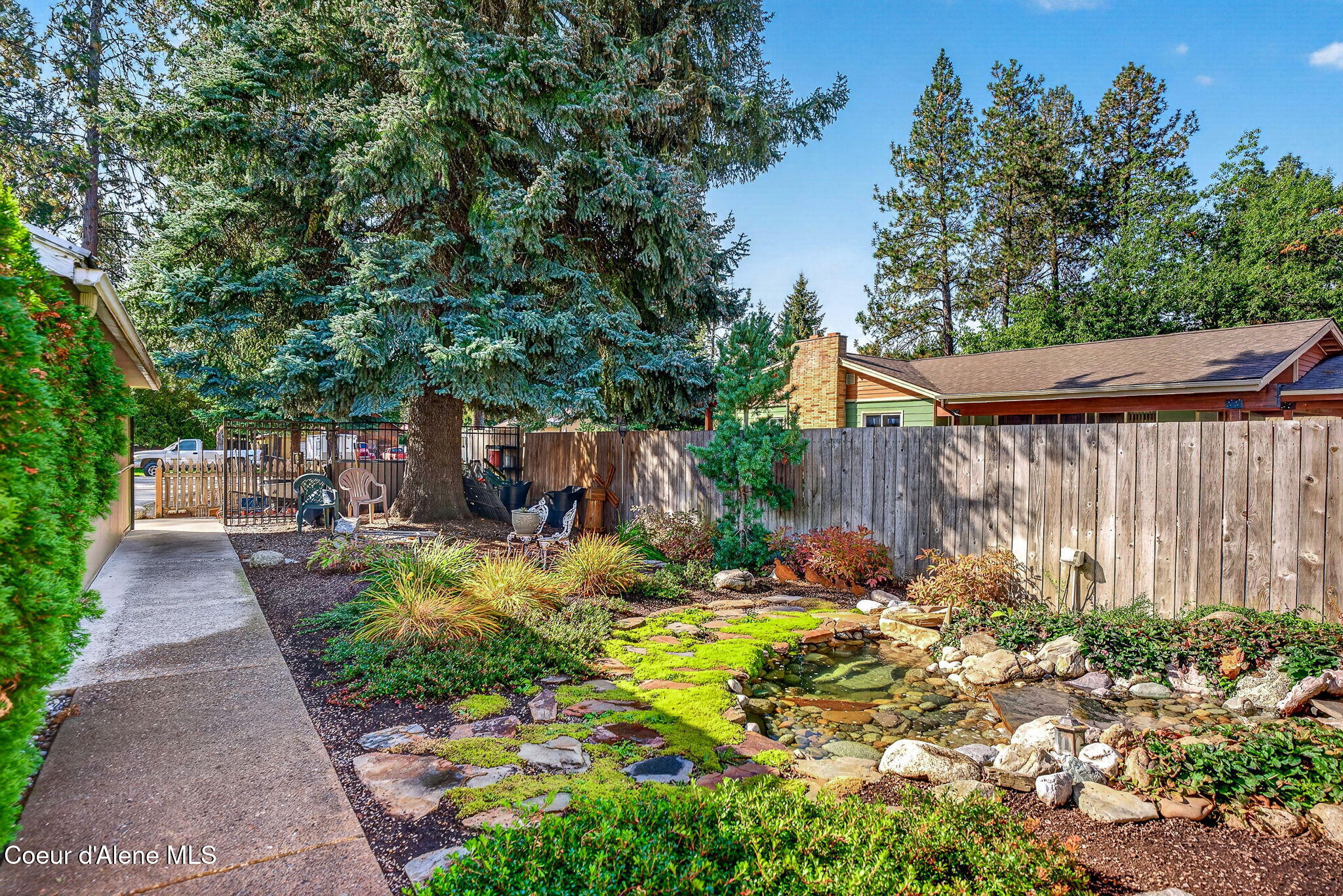 Landscaped backyard with a rock-edged pond, stepping stones, and mature evergreens.