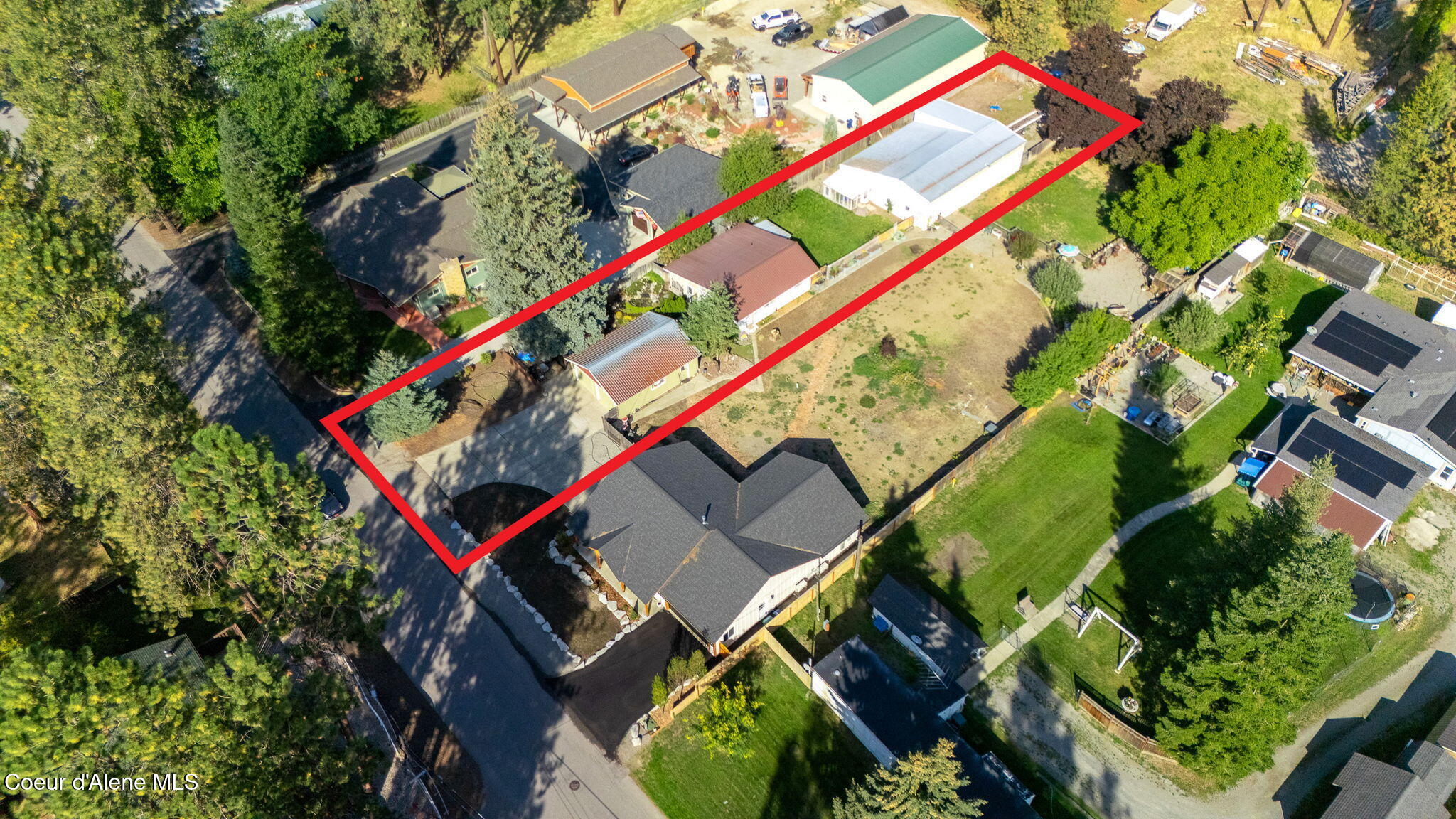 Aerial view of a long property outlined in red, with several buildings, an open yard, and mature trees.