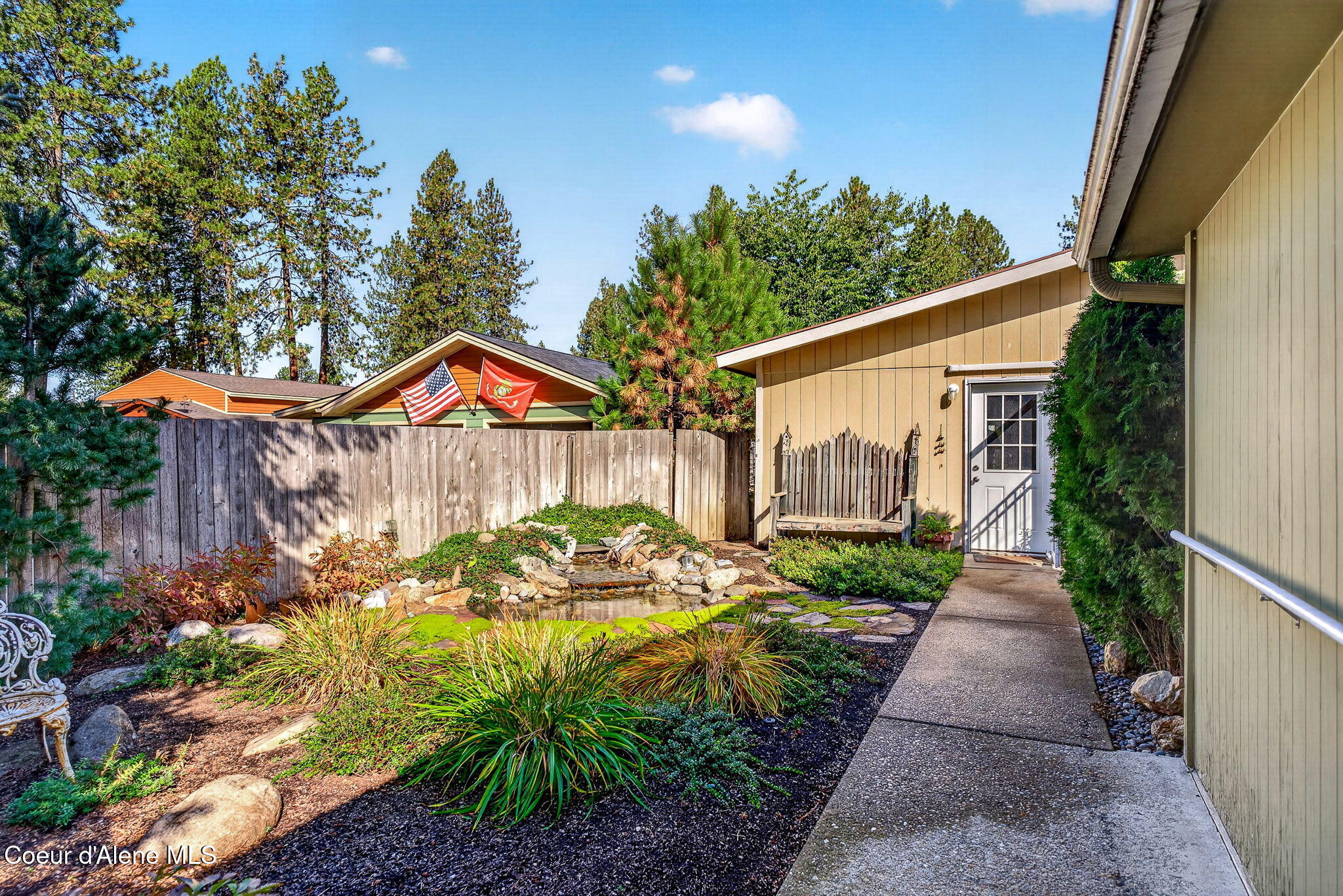 Landscaped side courtyard with a small rock-edged pond, garden path, and bench beside the house.