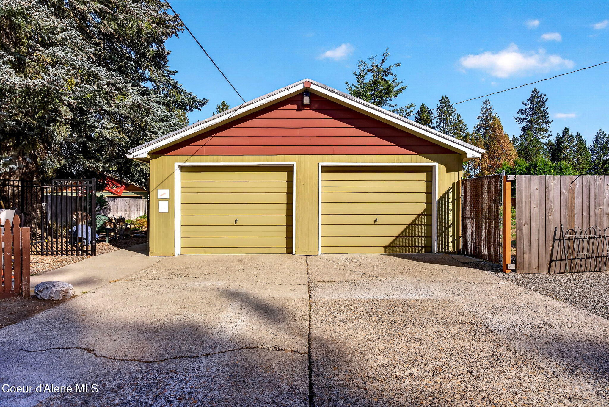 Detached two-car garage with yellow siding, red gable, and a wide concrete driveway.